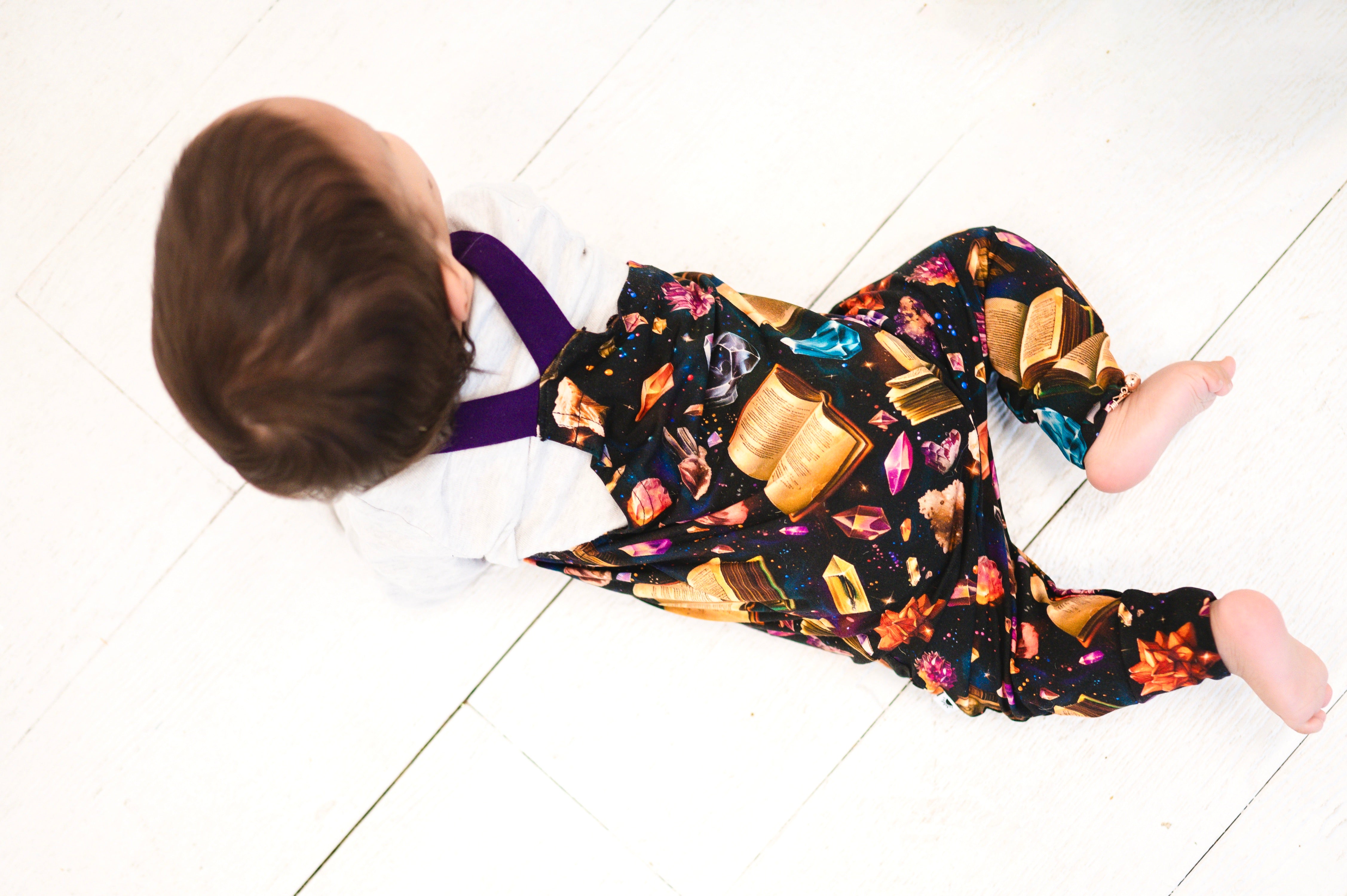Overalls with a crystal and book print and purple straps.