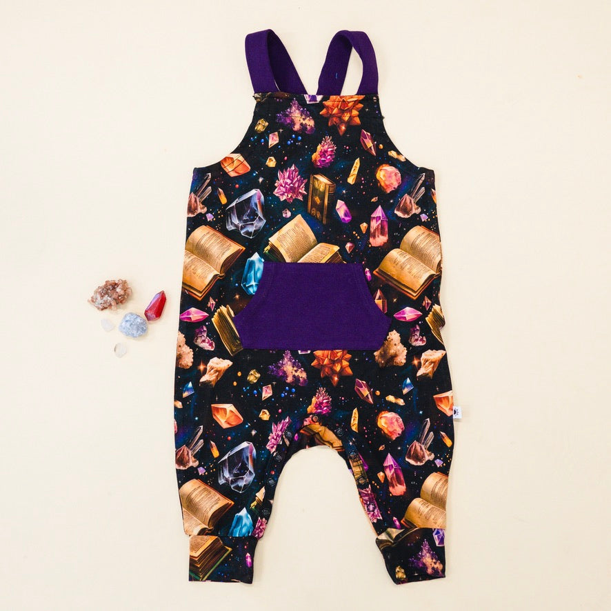 Overalls with a crystal and book print and a purple pocket.