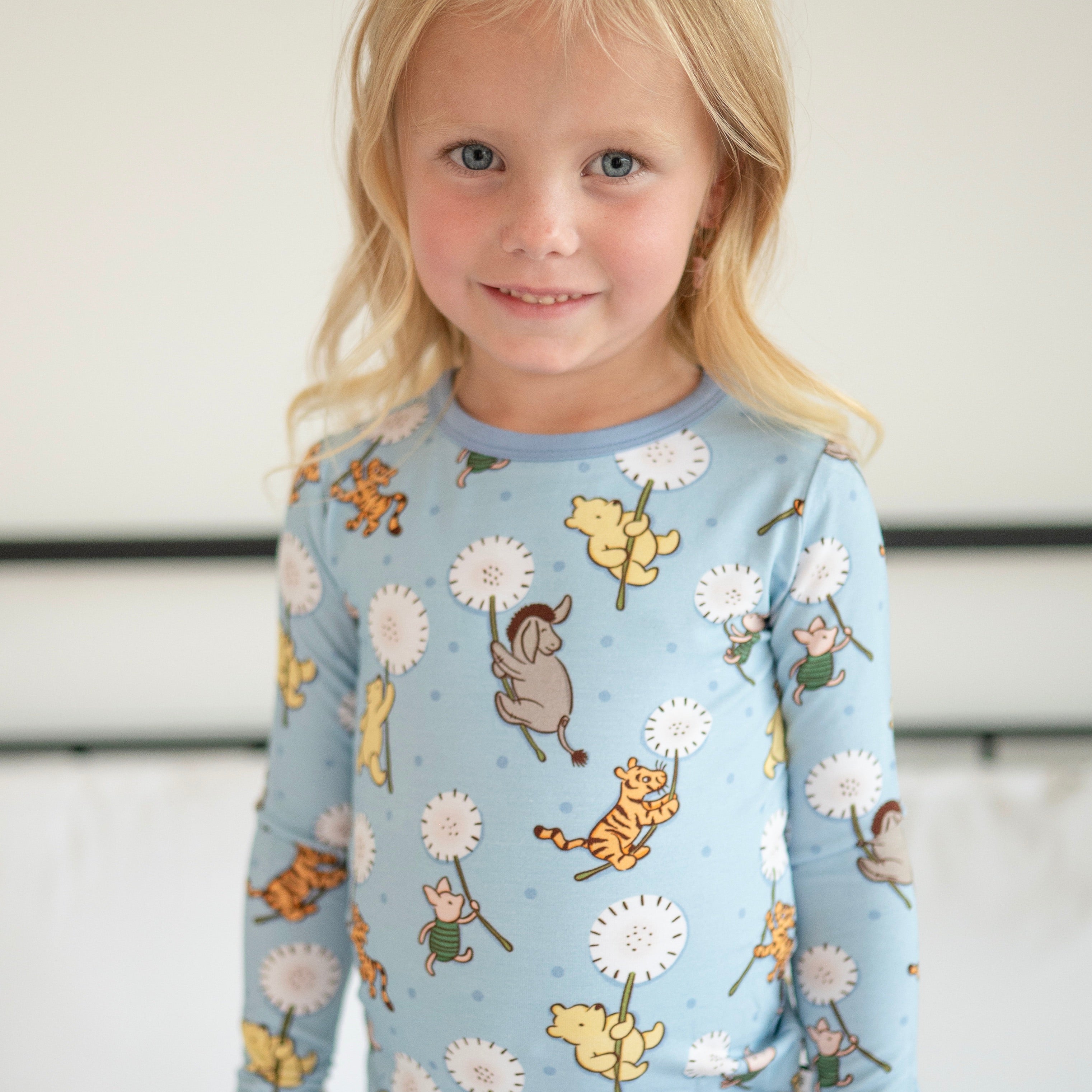 A young girl smiles wearing a light blue long-sleeved pajama top with a Winnie the Pooh character print.