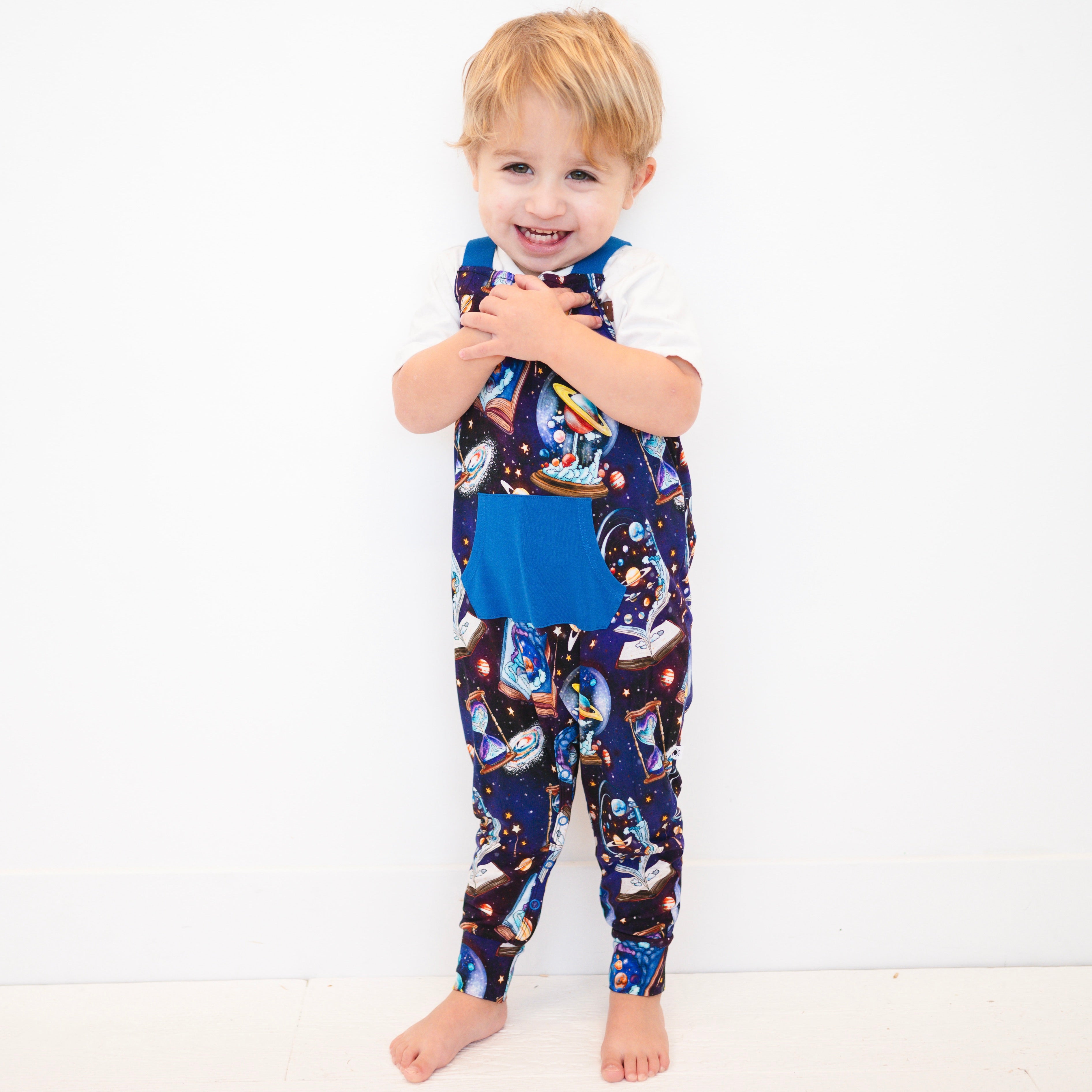 Toddler boy wearing blue overalls with a space-time continuum print.