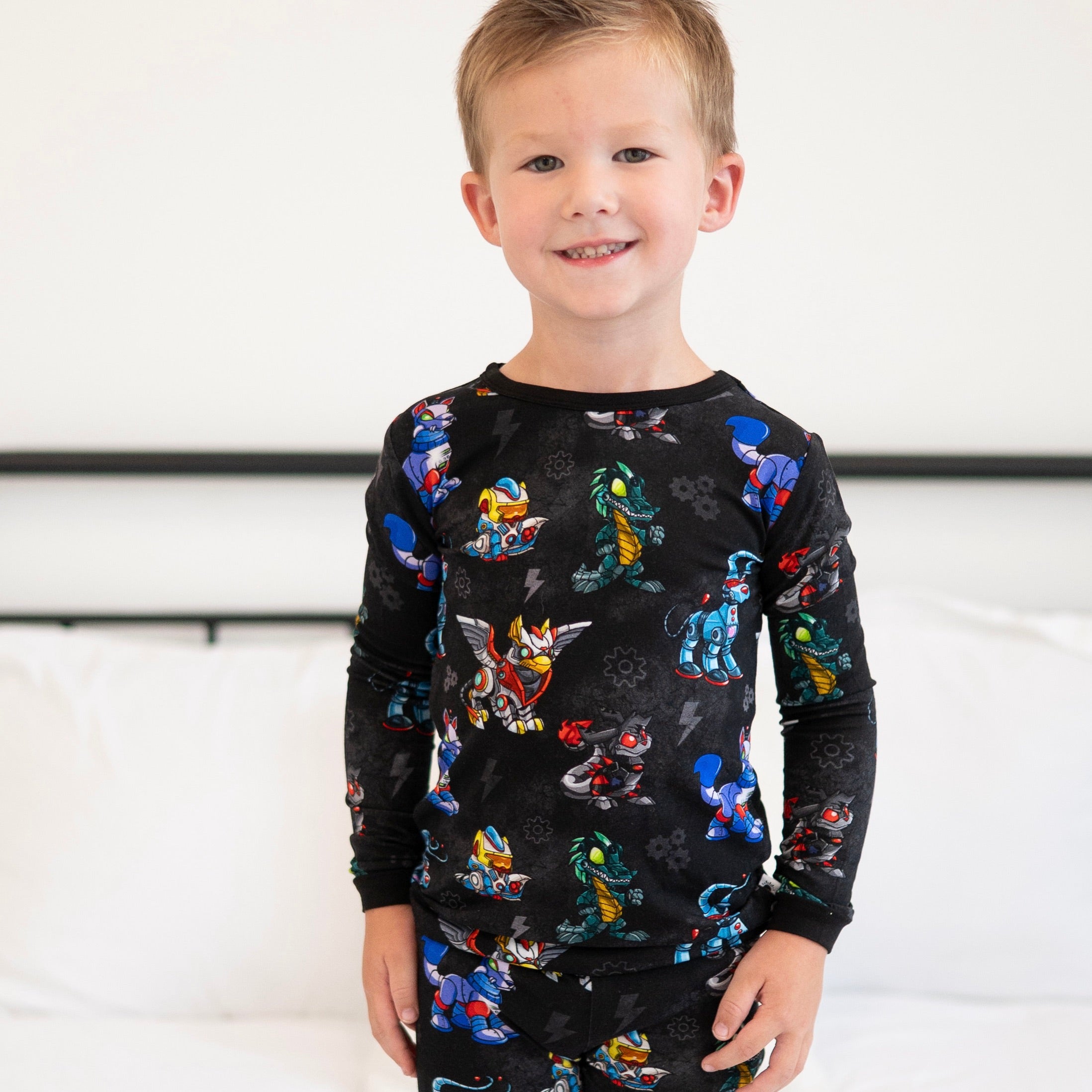 A young boy smiles wearing black pajamas with a robot and creature print.
