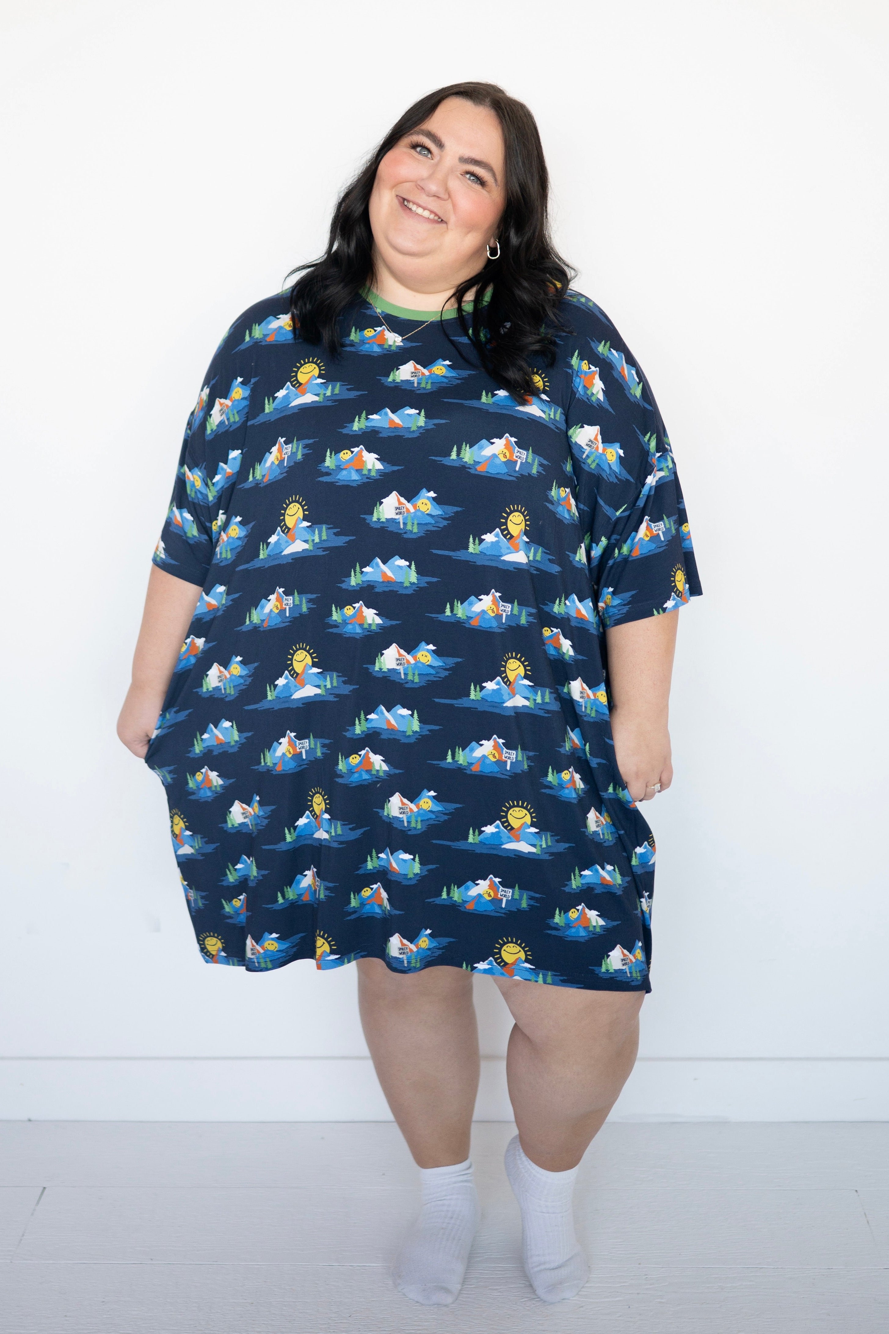 A woman wears a navy blue oversized t-shirt dress with a Mount SmileyWorld print and white socks.