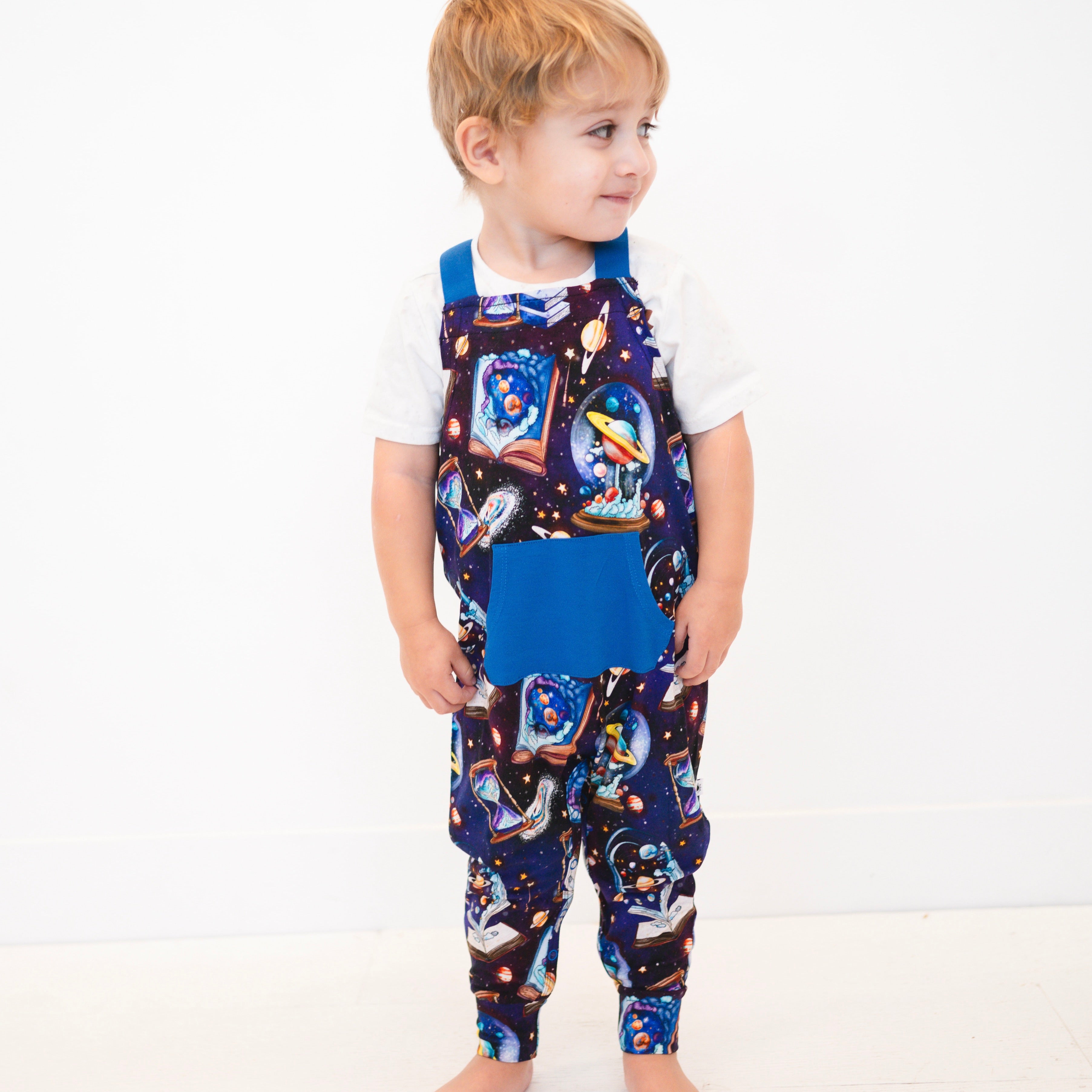 A young boy wears blue overalls with a space-time continuum print.
