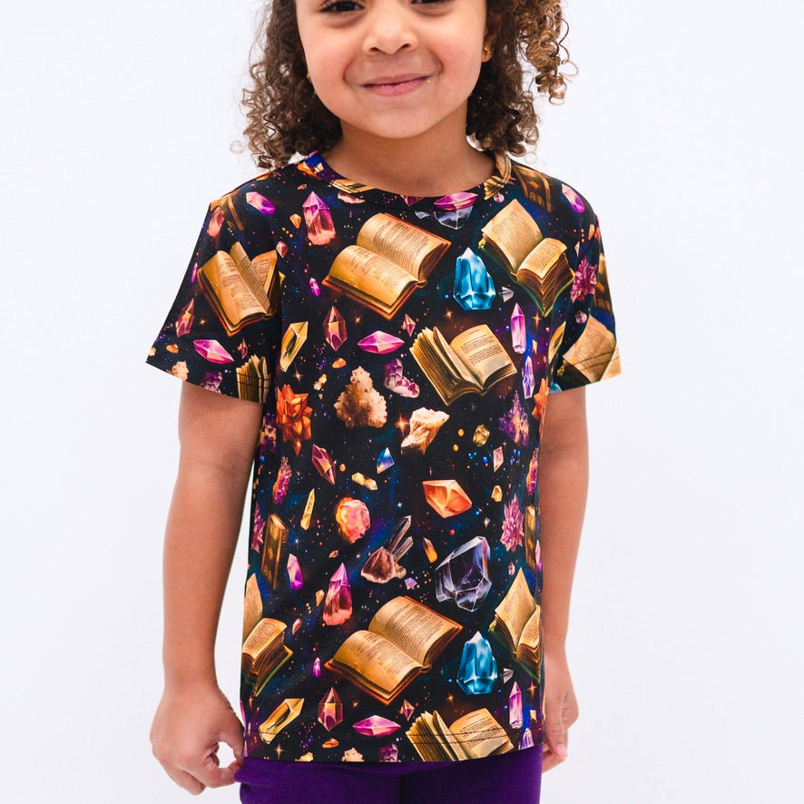 T-shirt with a black background featuring an all-over print of open books and colorful crystals.