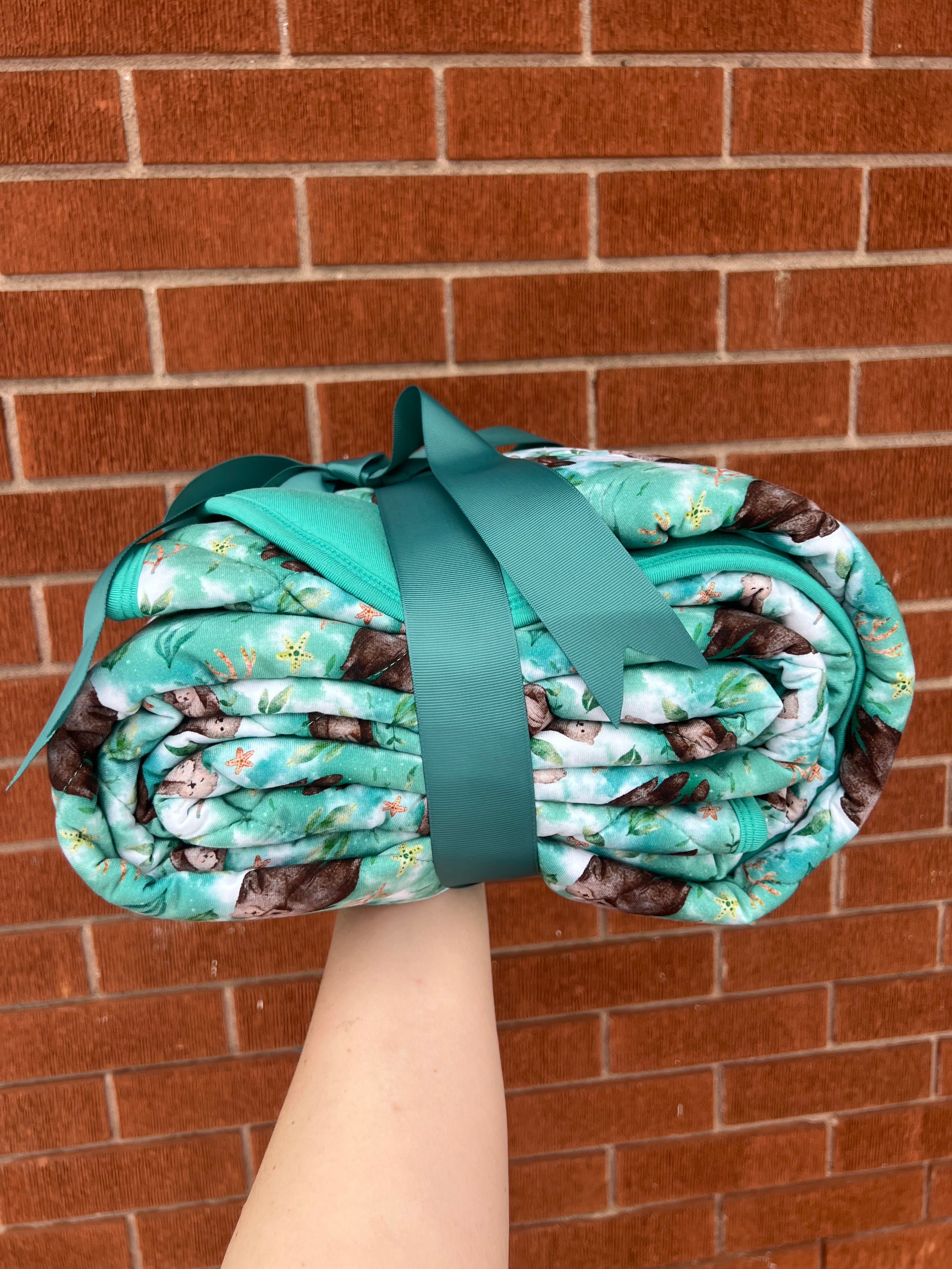 Rolled up bamboo blanket with an otter print, tied with a teal ribbon.