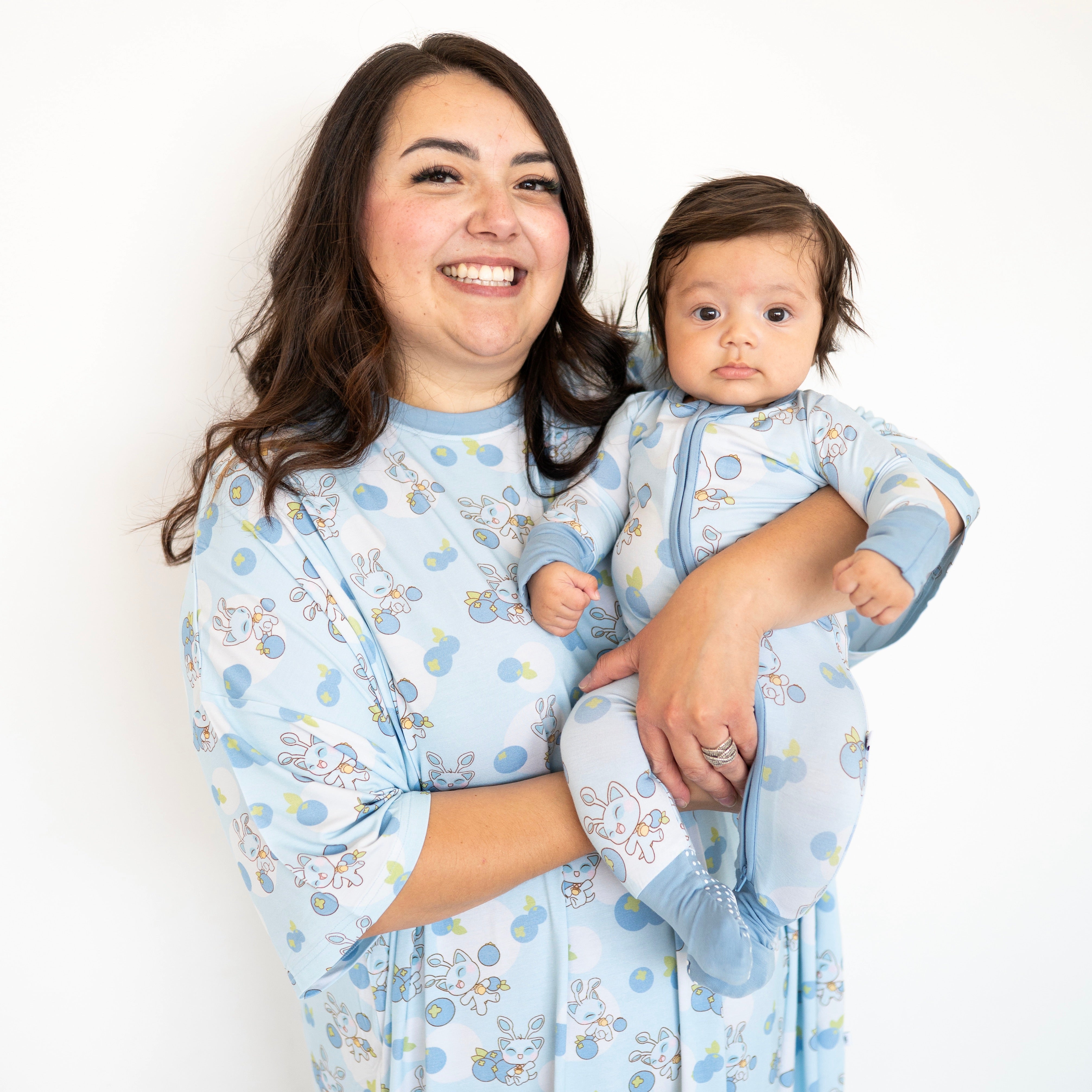 A woman holds a baby, both wearing matching blue Neopets blueberry pajamas.