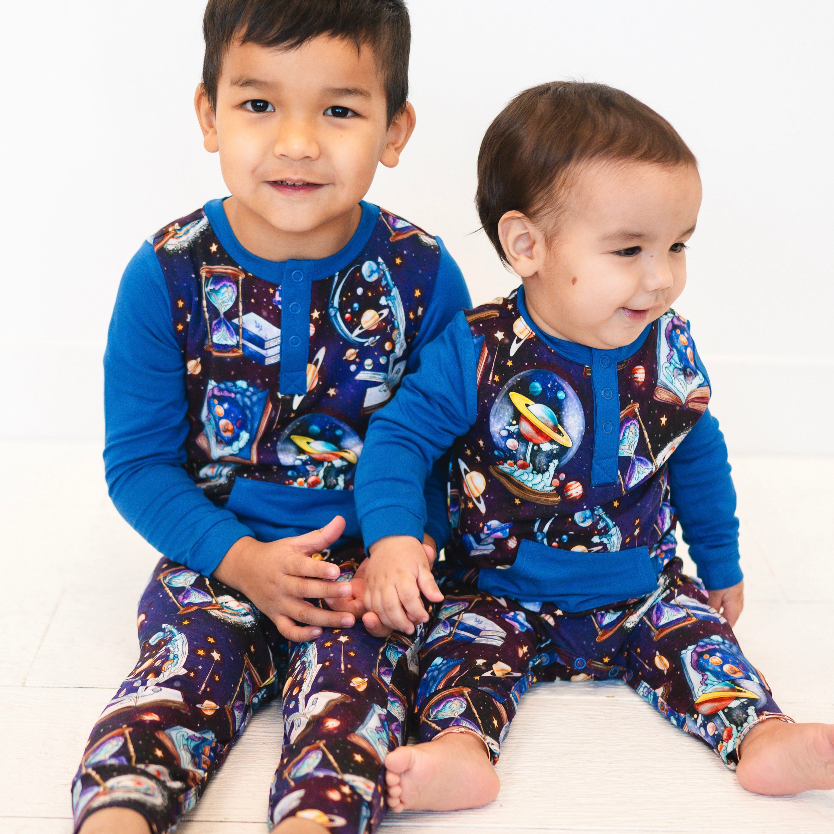 Two young boys in matching blue and space-themed rompers.