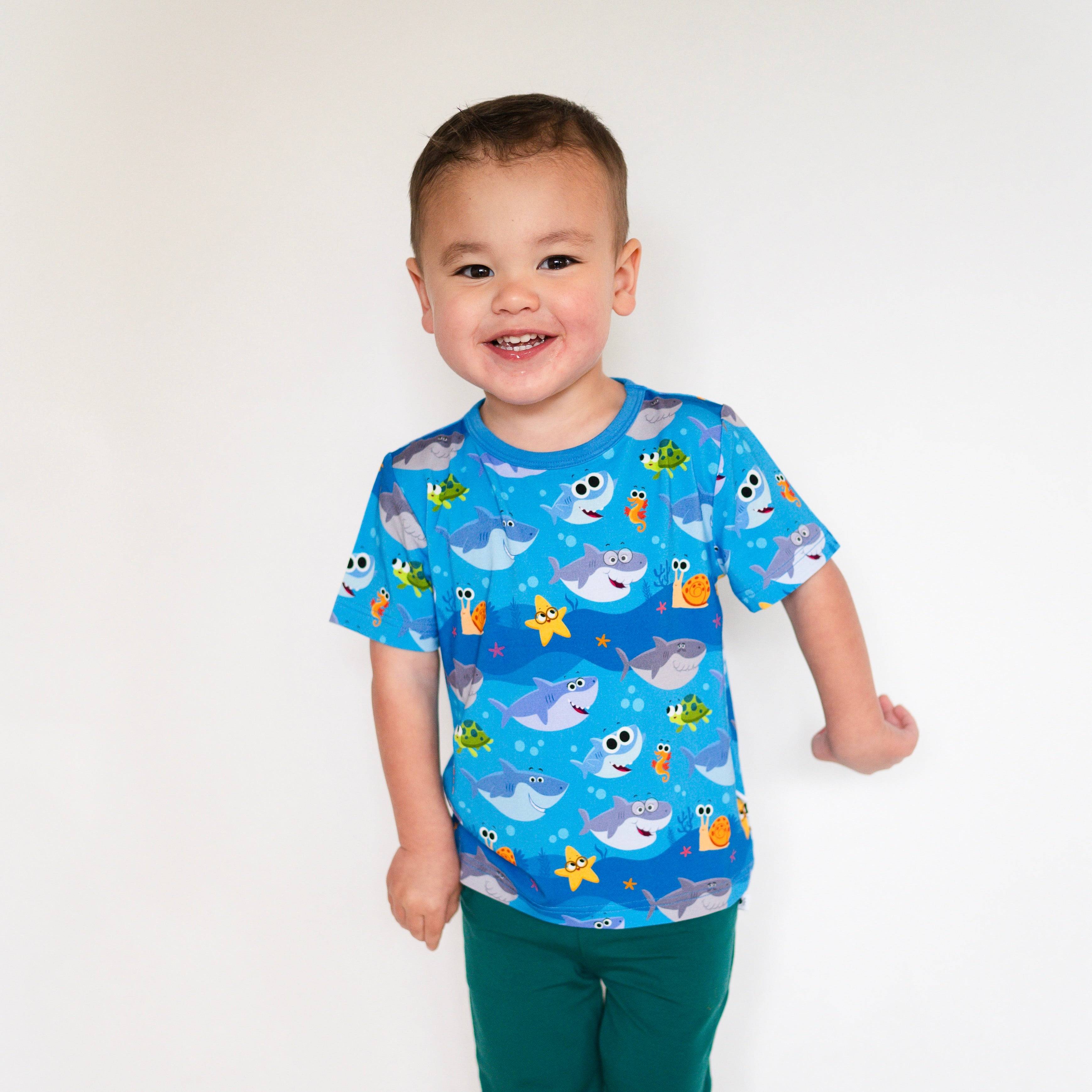 A young boy smiles wearing a blue t-shirt with a Baby Shark print.