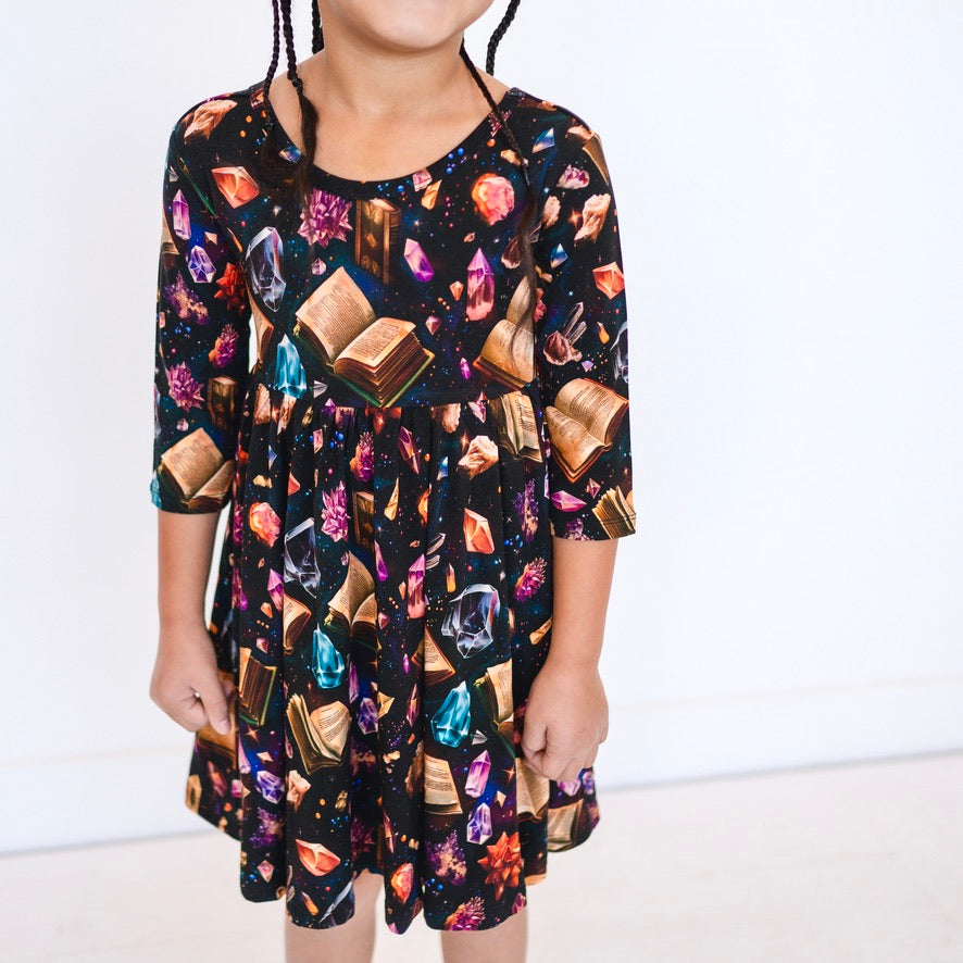A black 3/4 sleeve dress with a print of books and crystals.
