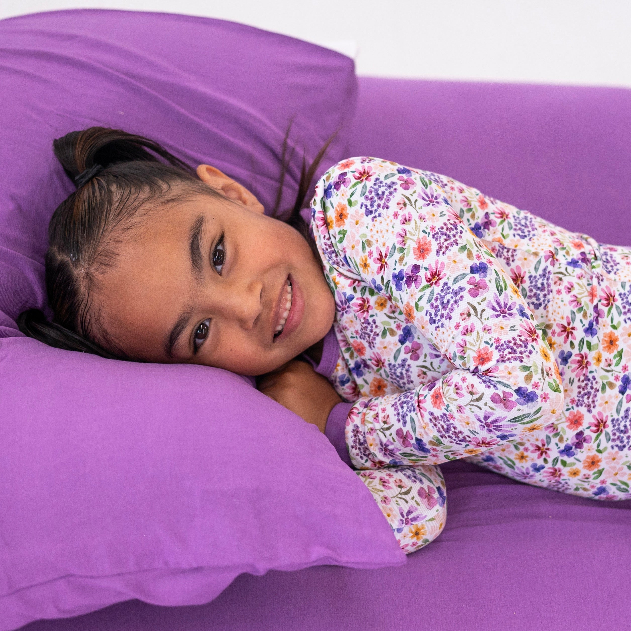 A young girl in floral pajamas lies on a purple surface.