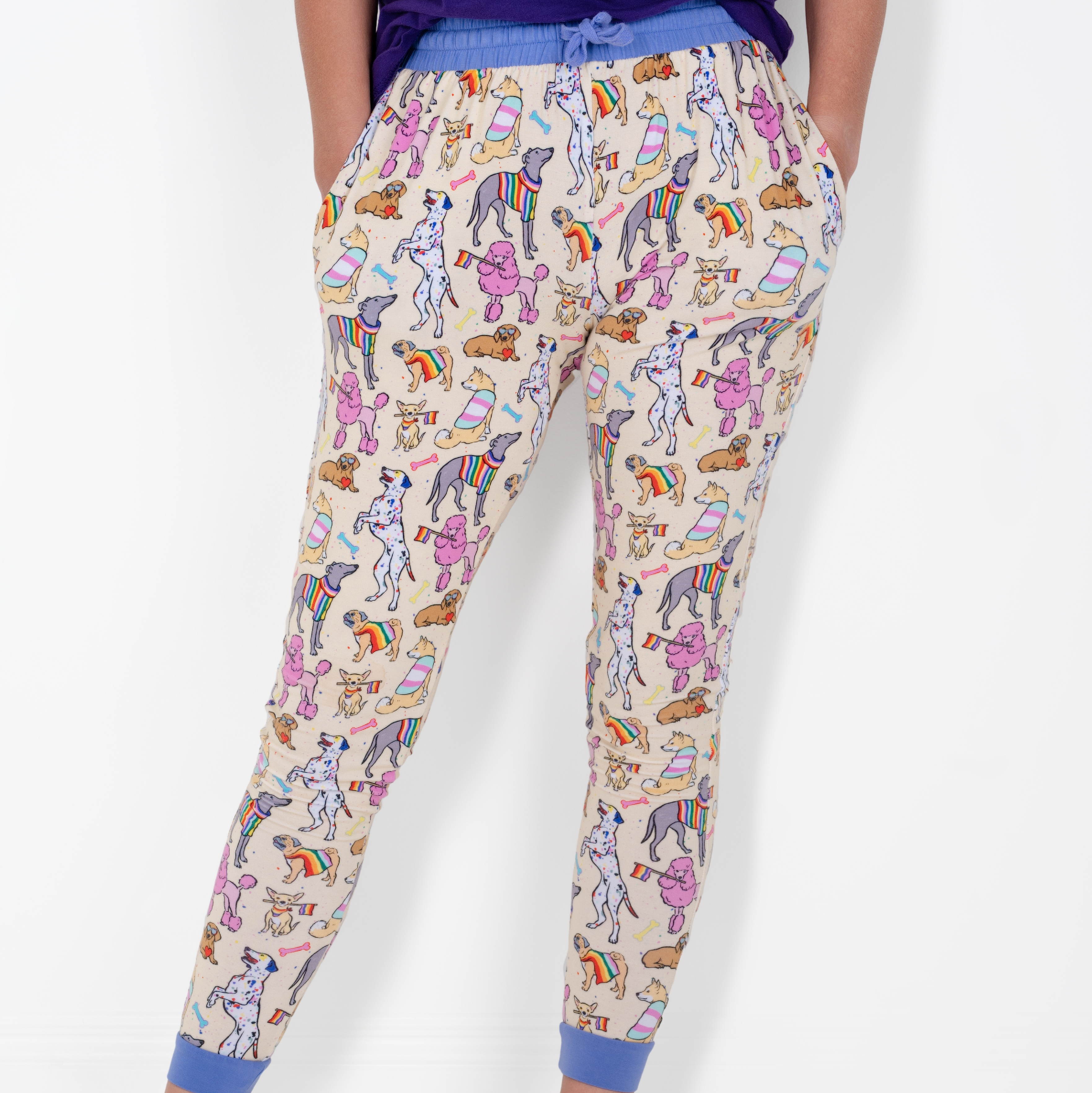 Adult joggers with a cream background and a print of various dogs wearing rainbow-colored accessories.