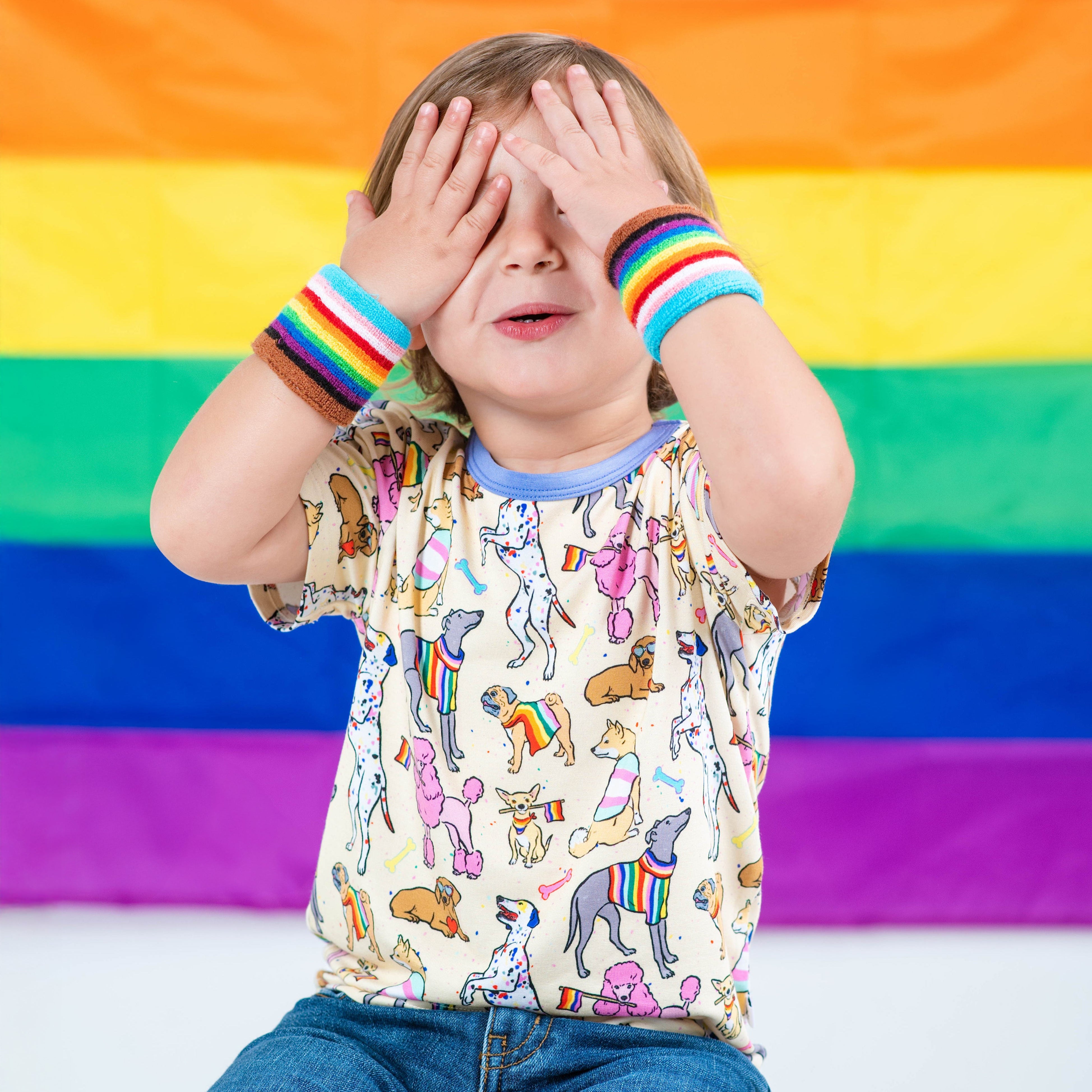 A child wears a t-shirt with a rainbow dog print and rainbow wristbands.