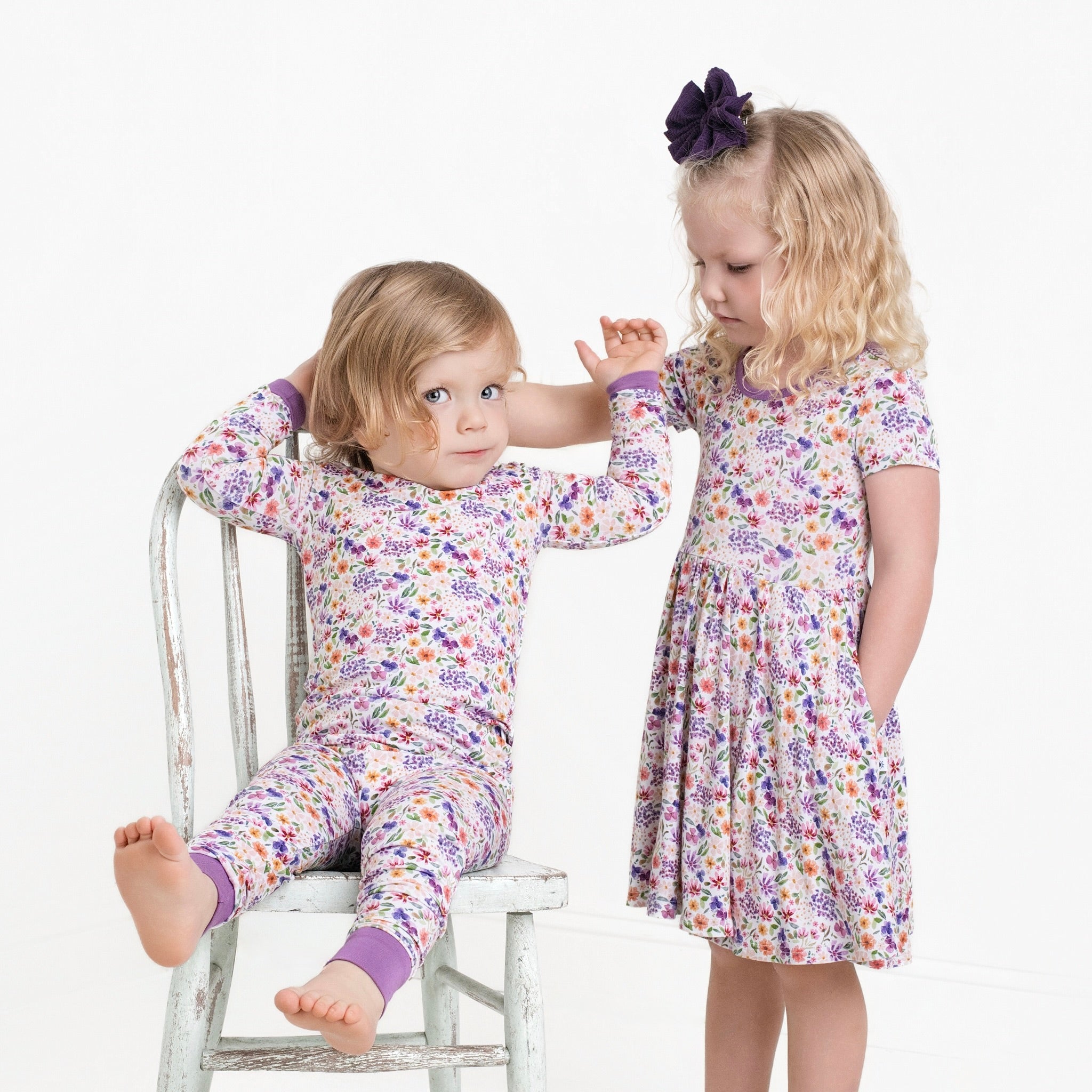 Two young girls in floral pajamas, one sitting on a chair and the other standing.
