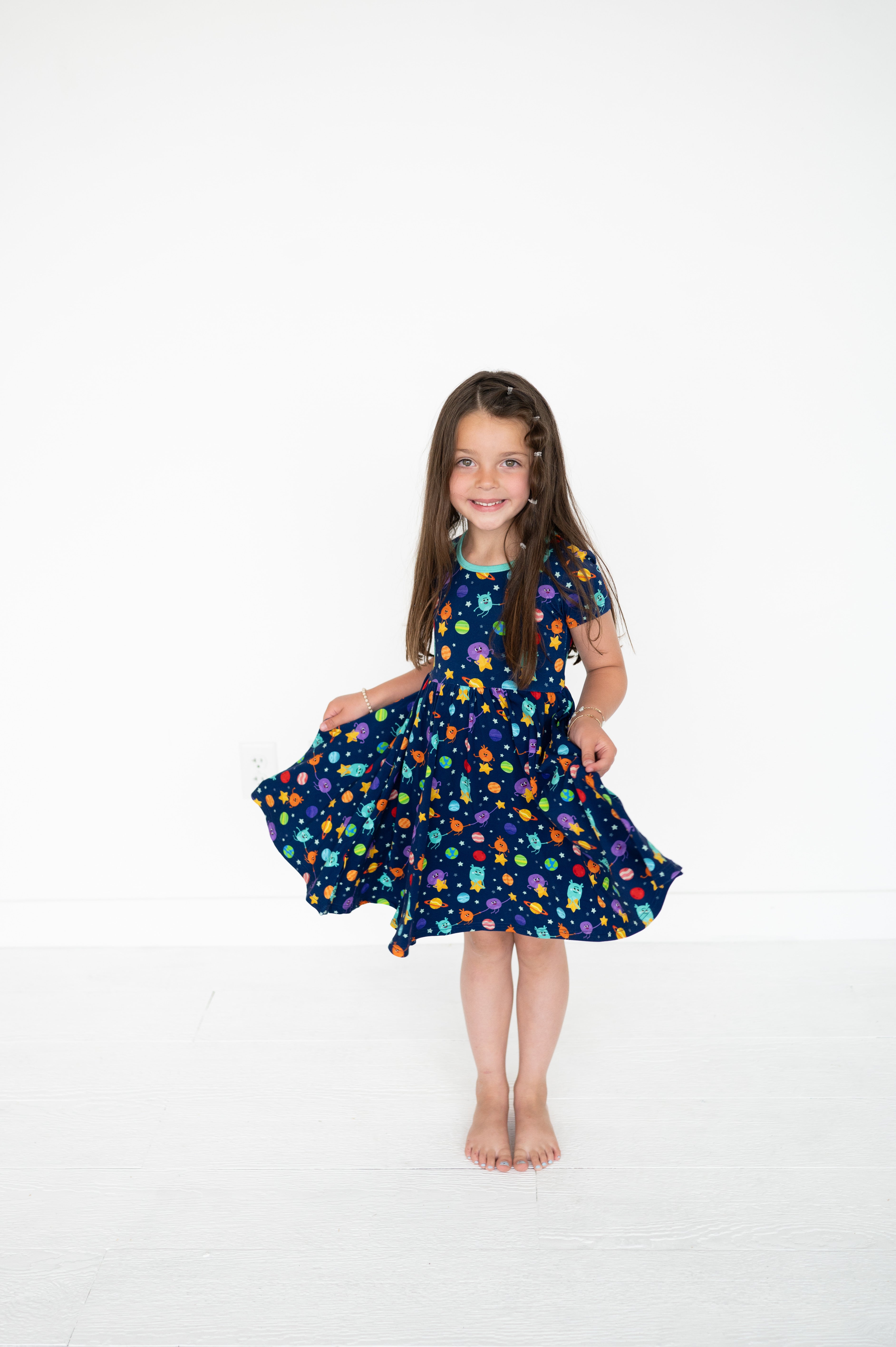A young girl in a navy blue dress with a colorful space print.