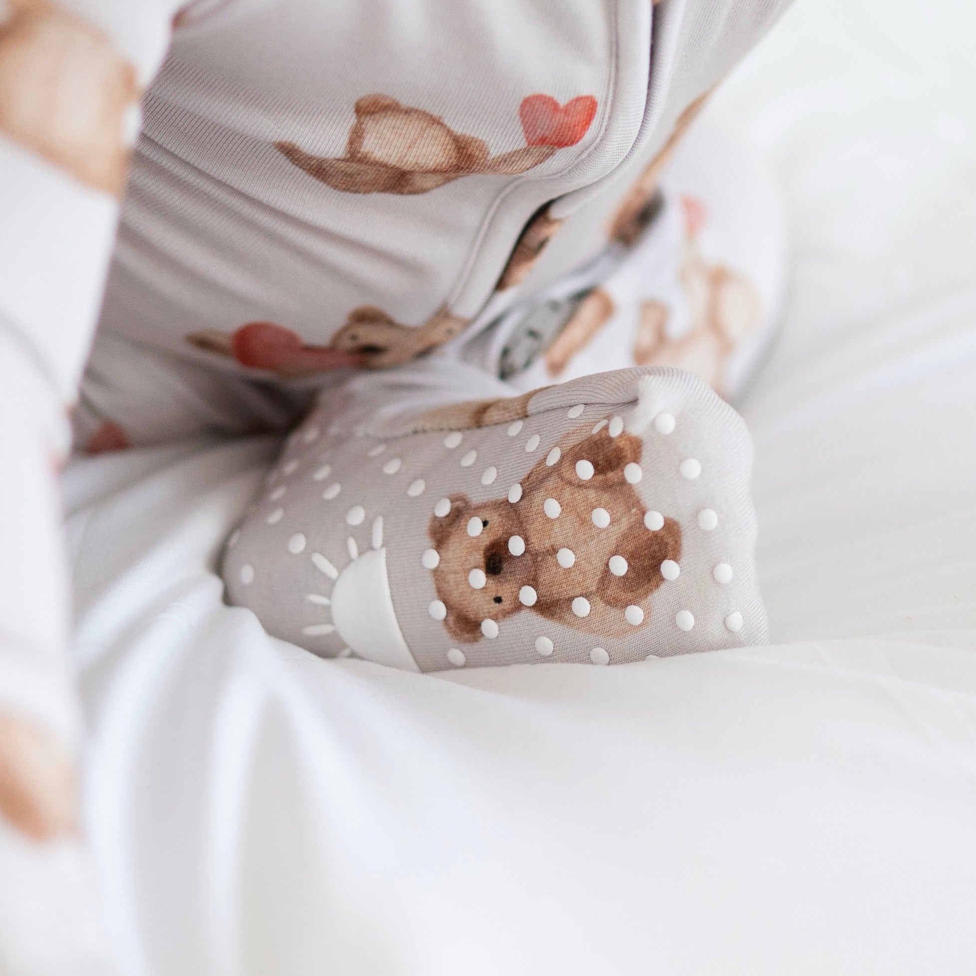A baby's foot in a grey pajama with a teddy bear print and white polka dots.
