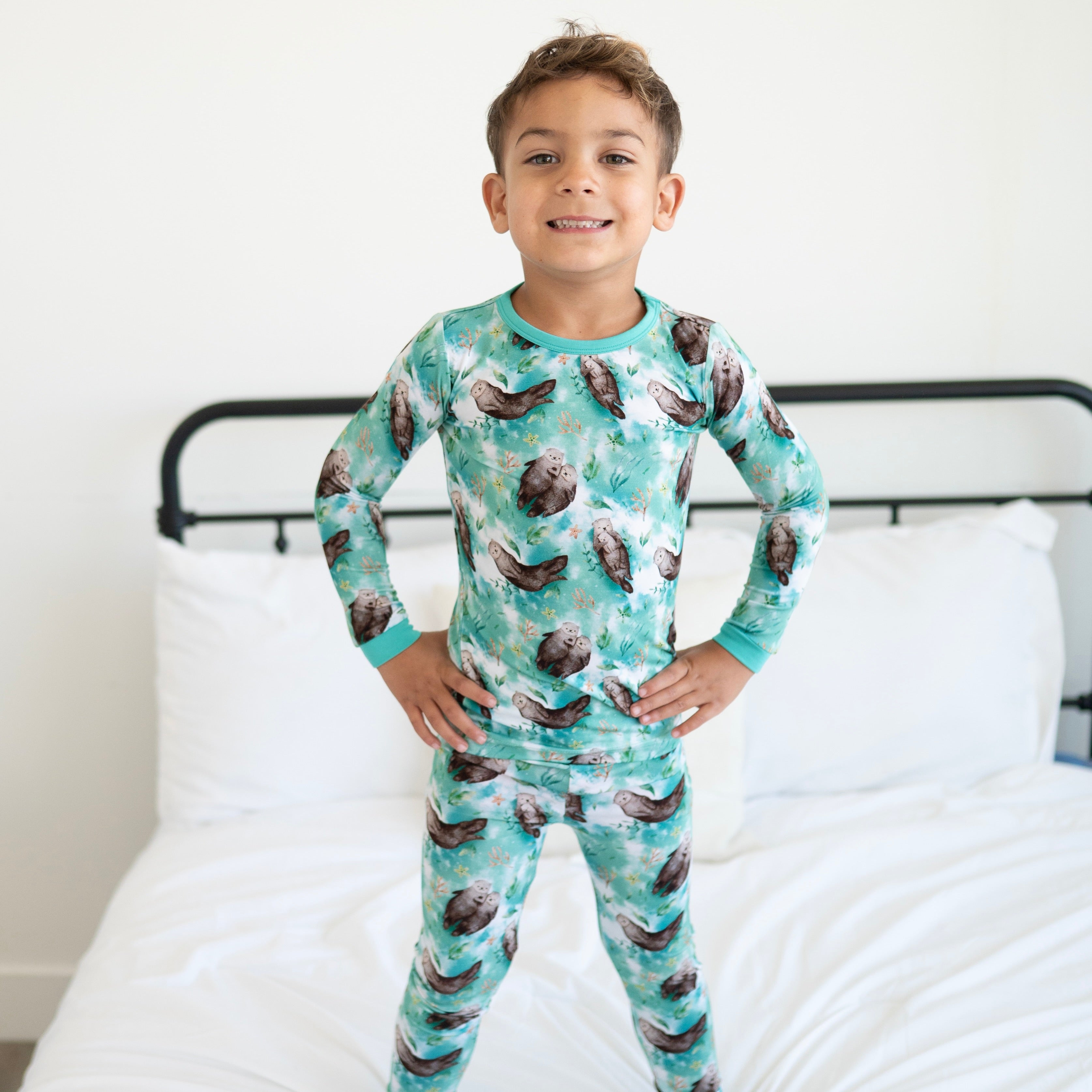 A young boy wears a long-sleeved pajama set with an otter print.