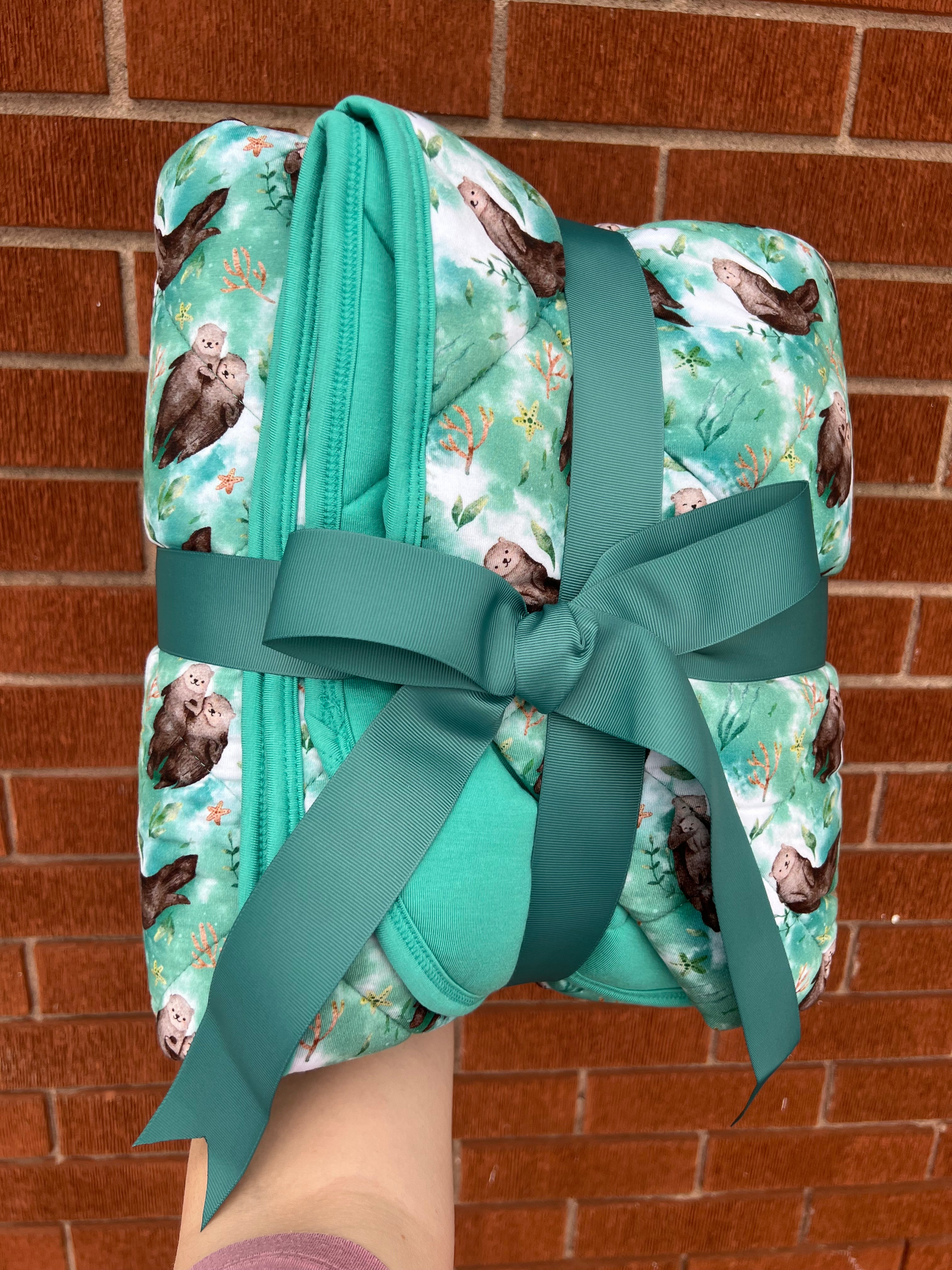 A folded bamboo blanket with an otter print, tied with a green ribbon.