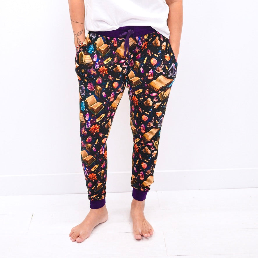 Women's black joggers with a crystal and book print and purple cuffs.