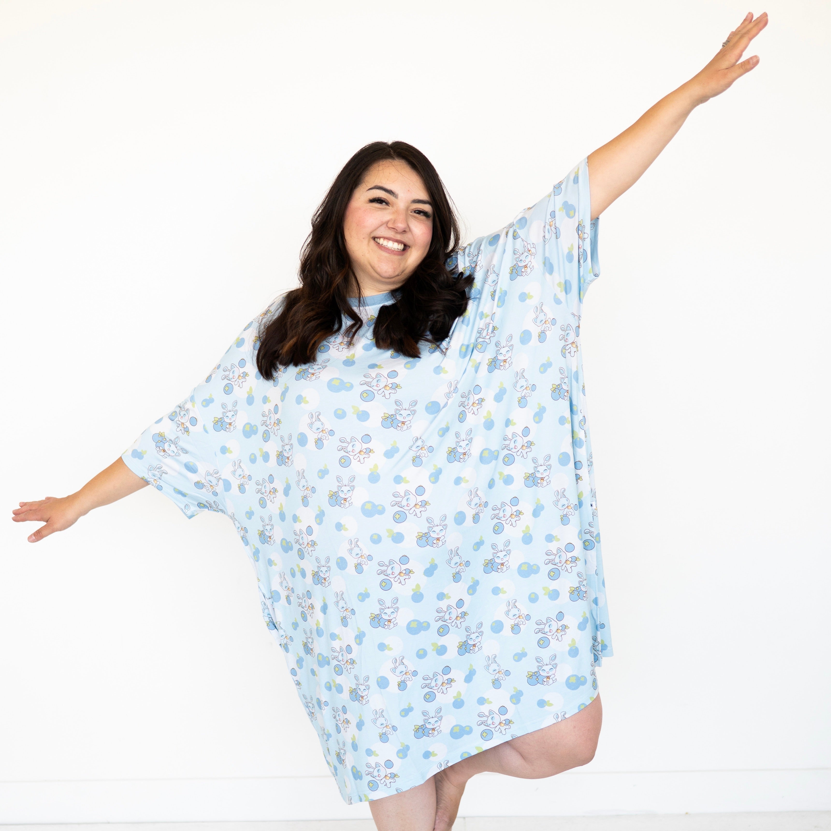 A woman wears a light blue oversized sleep tee with a blueberry and Neopets® Blueberry Baby print.