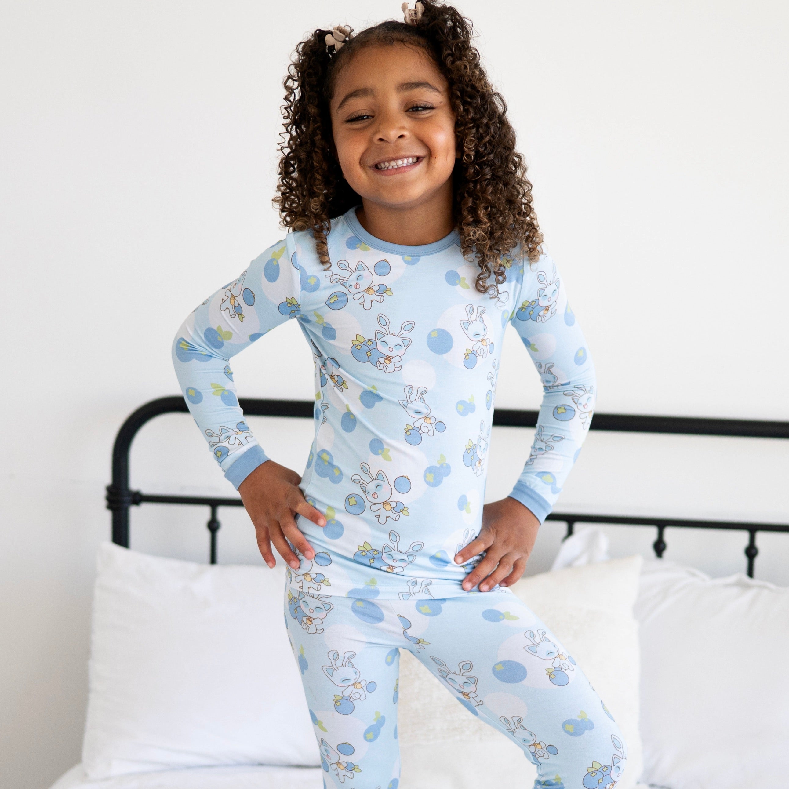 A young girl smiles in light blue pajamas with a blueberry and baby Neopets print.