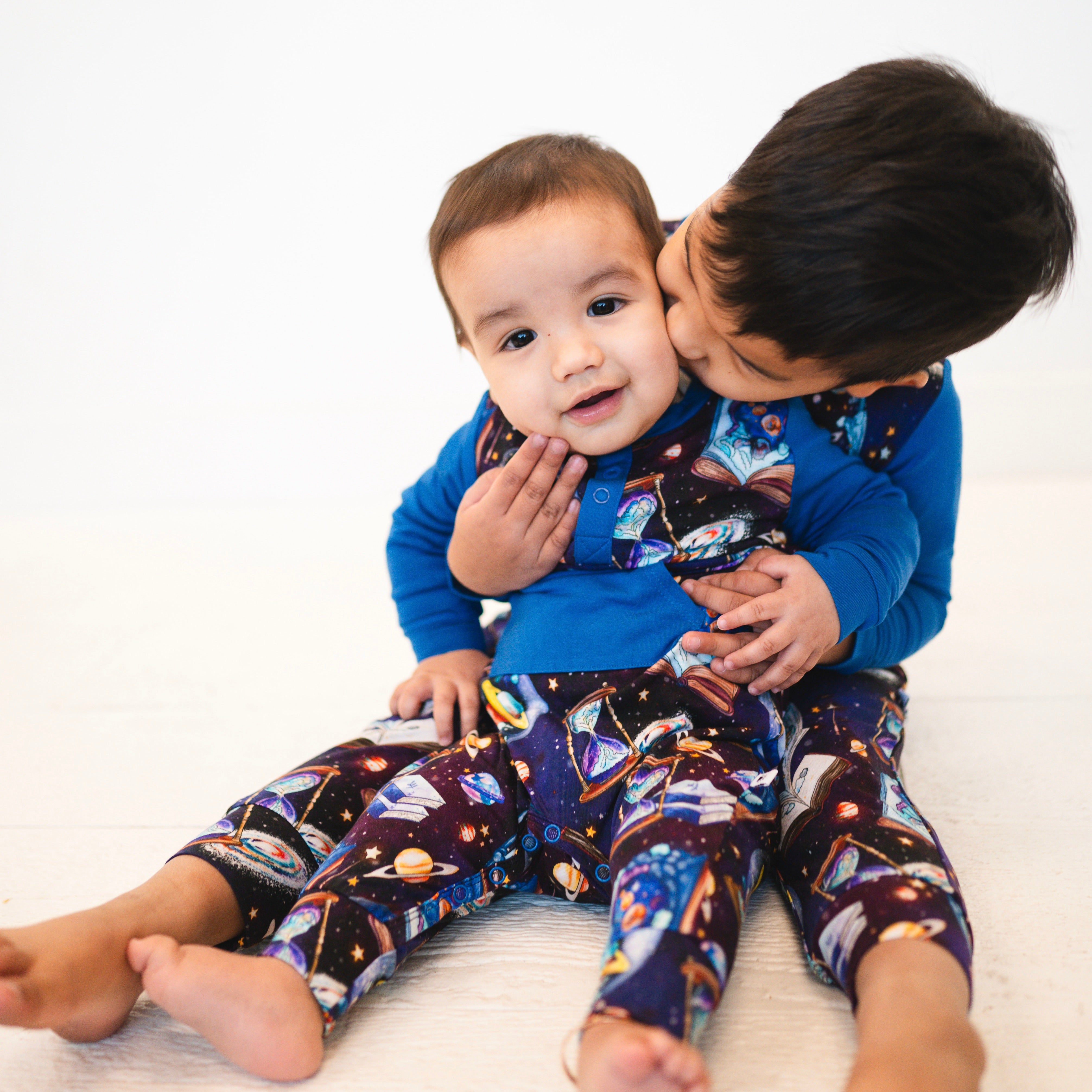 Two children in blue rompers with a space-time continuum print.