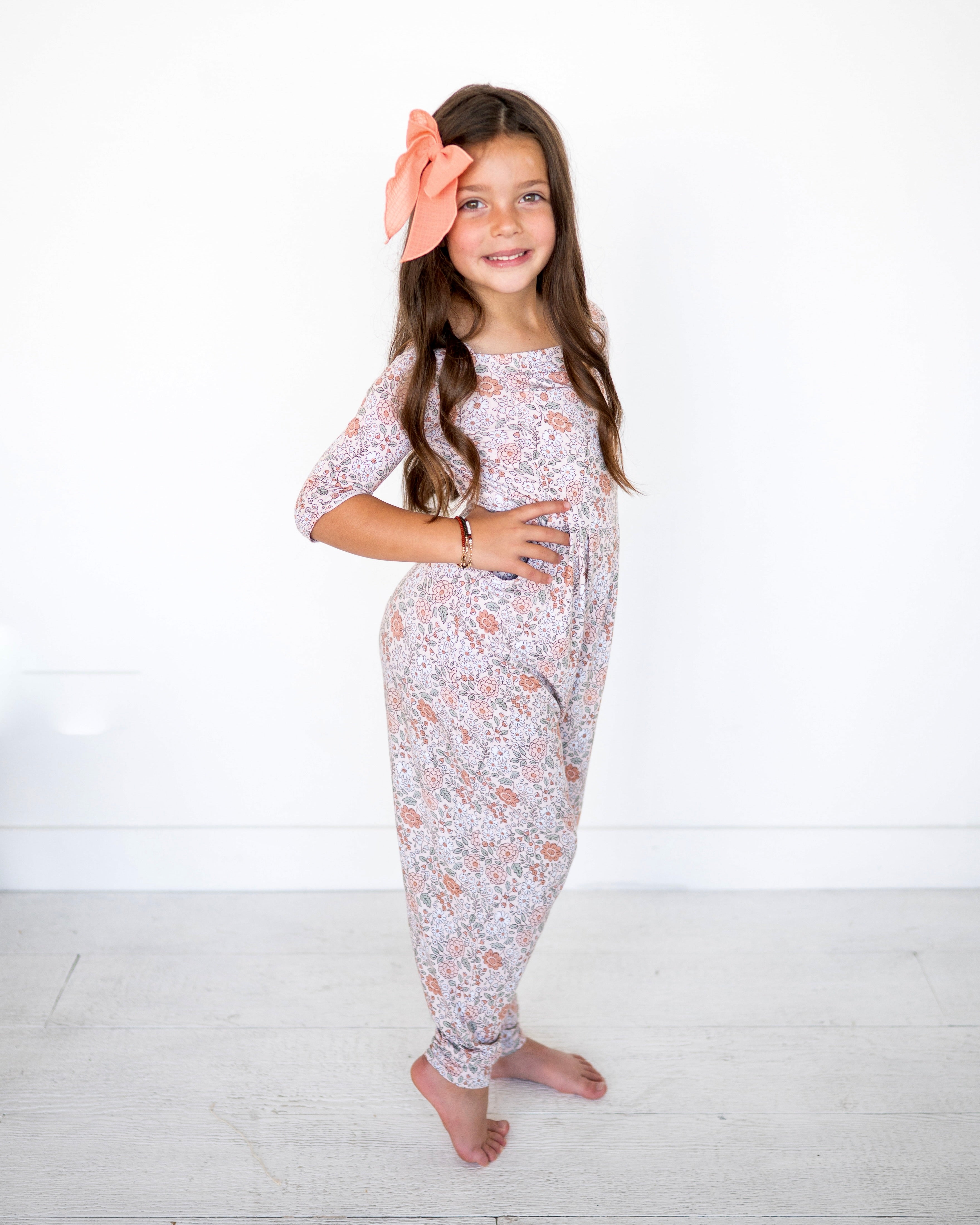 A young girl wears a vintage floral romper with a large peach bow in her hair.