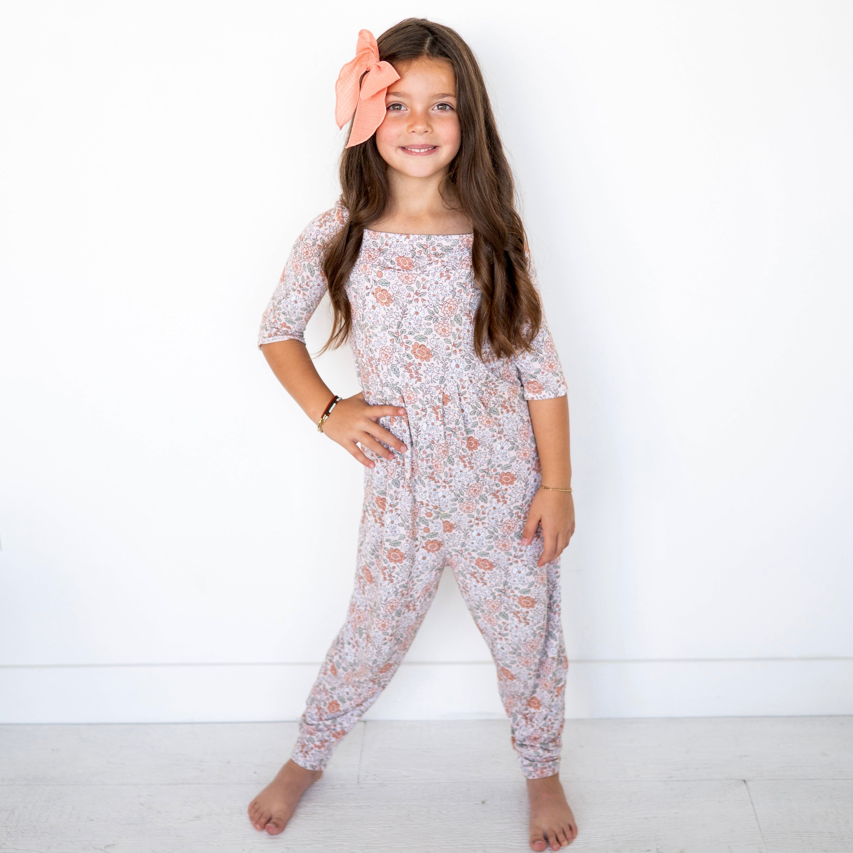 A young girl wears a vintage floral print romper with a peach bow in her hair.
