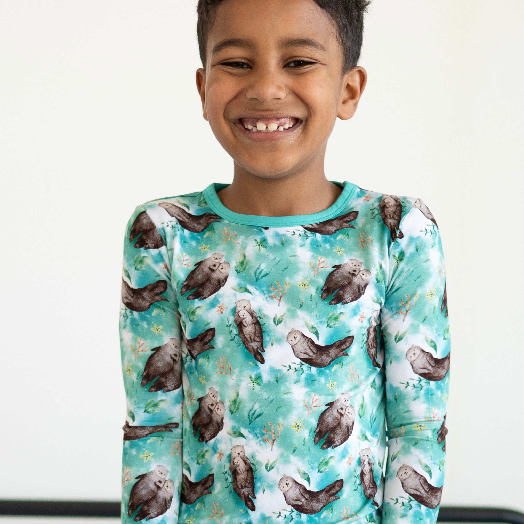 A young boy smiles wearing a long-sleeved pajama top with an otter print.