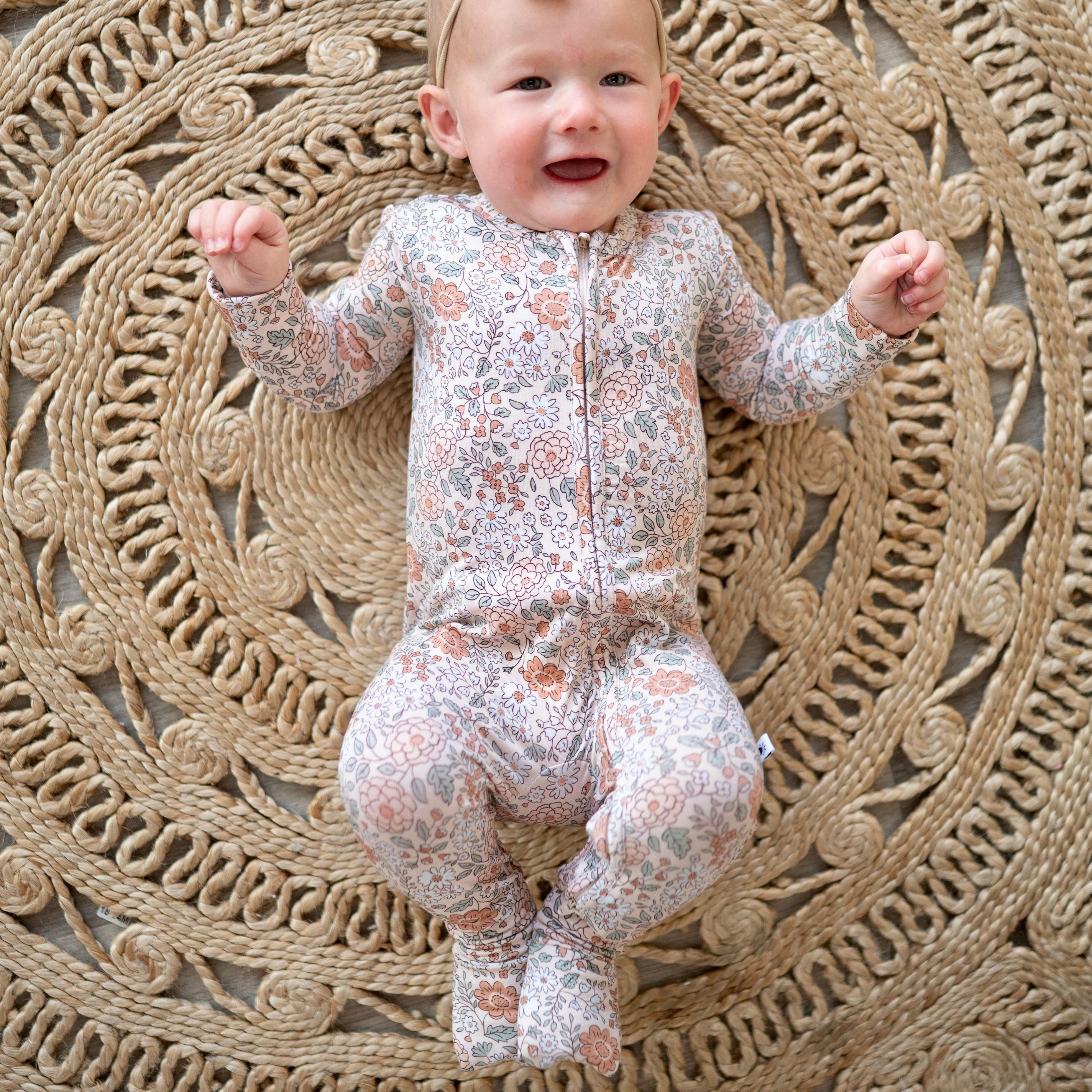 Baby in a vintage floral zip pajama on a jute rug.