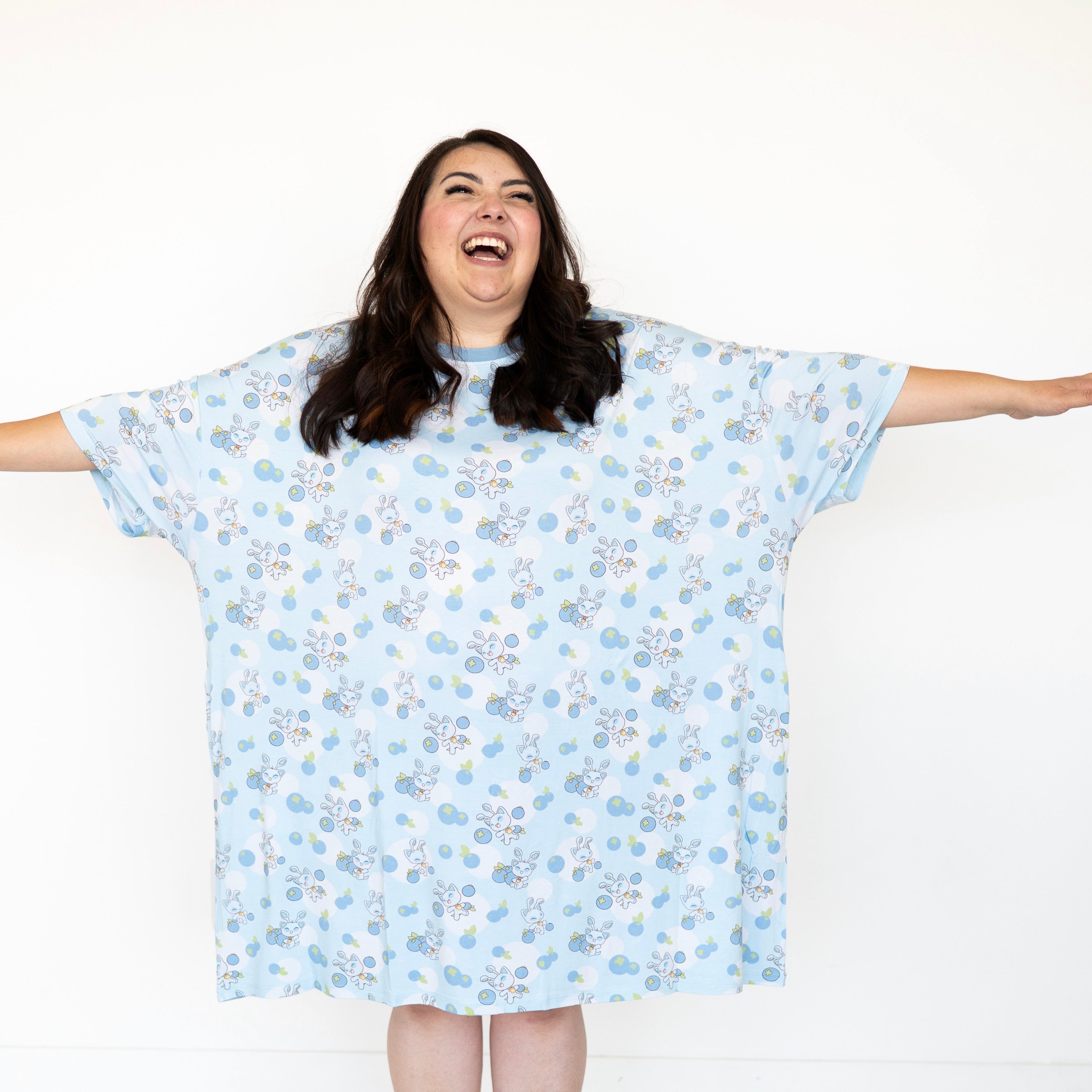 A woman laughs while wearing a light blue oversized sleep shirt with a blueberry and baby Neopets print.
