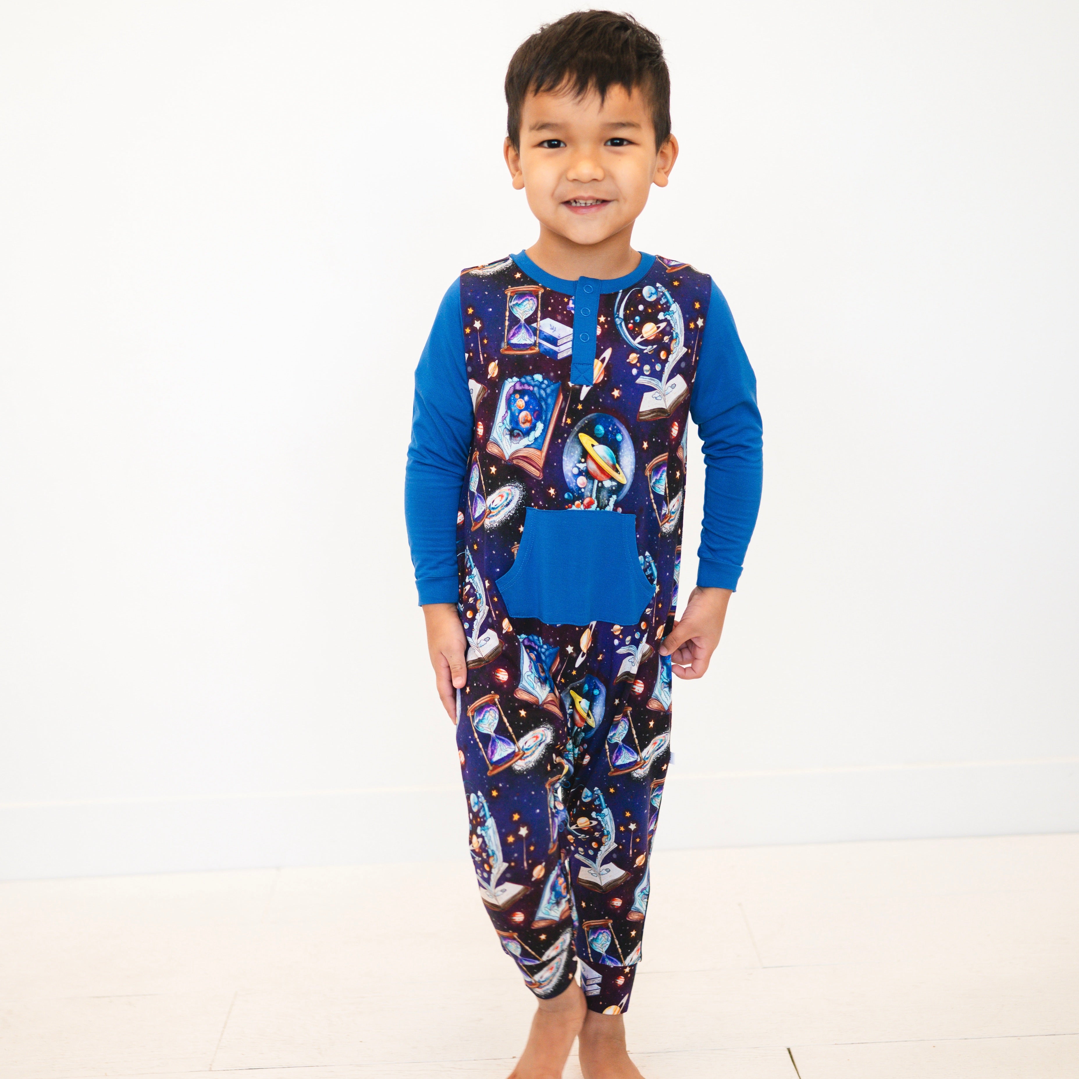 A young boy wears a blue and space-themed Henley romper.
