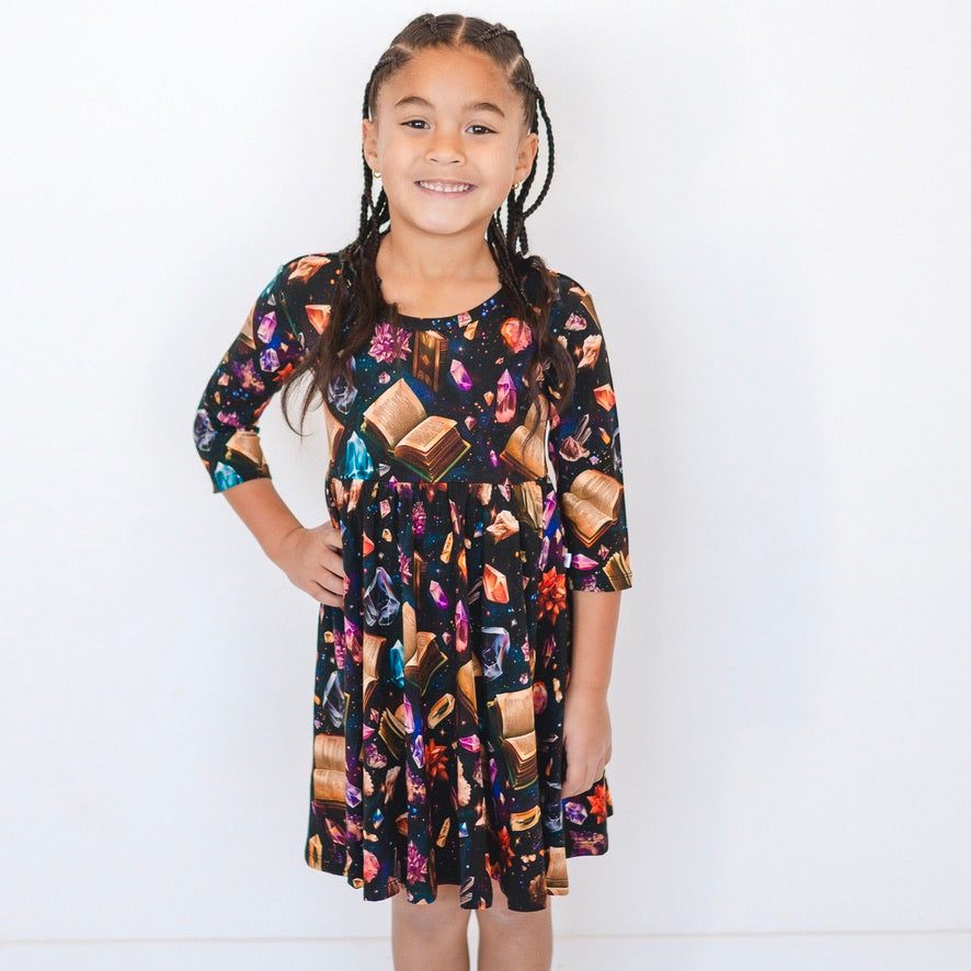 A girl wears a black 3/4 sleeve dress with a crystal and book print.