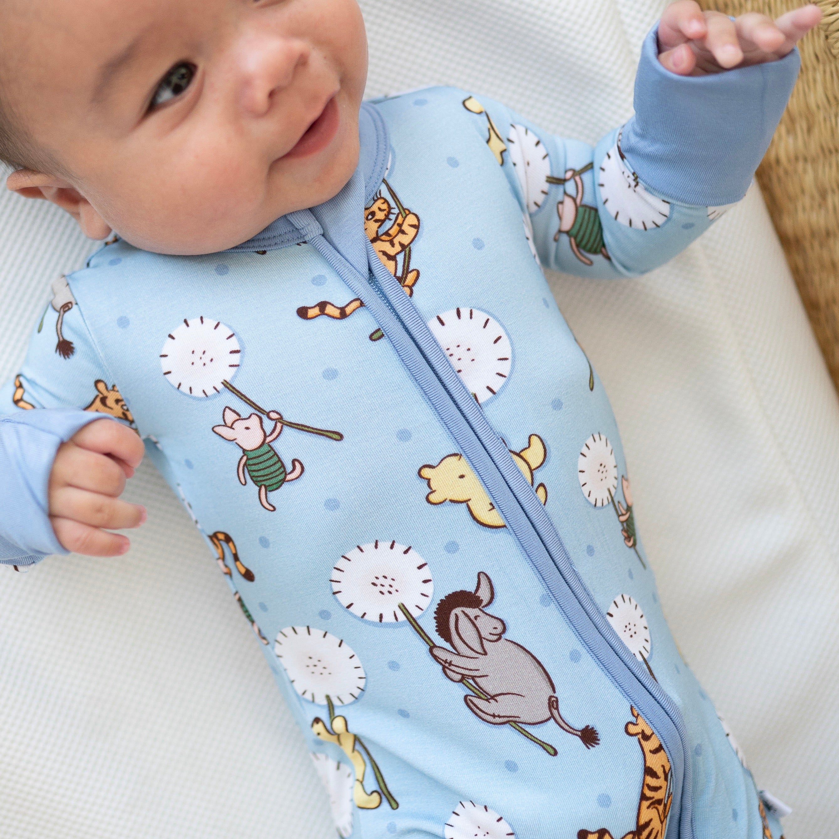 A baby wearing a light blue Winnie the Pooh print footed pajama.