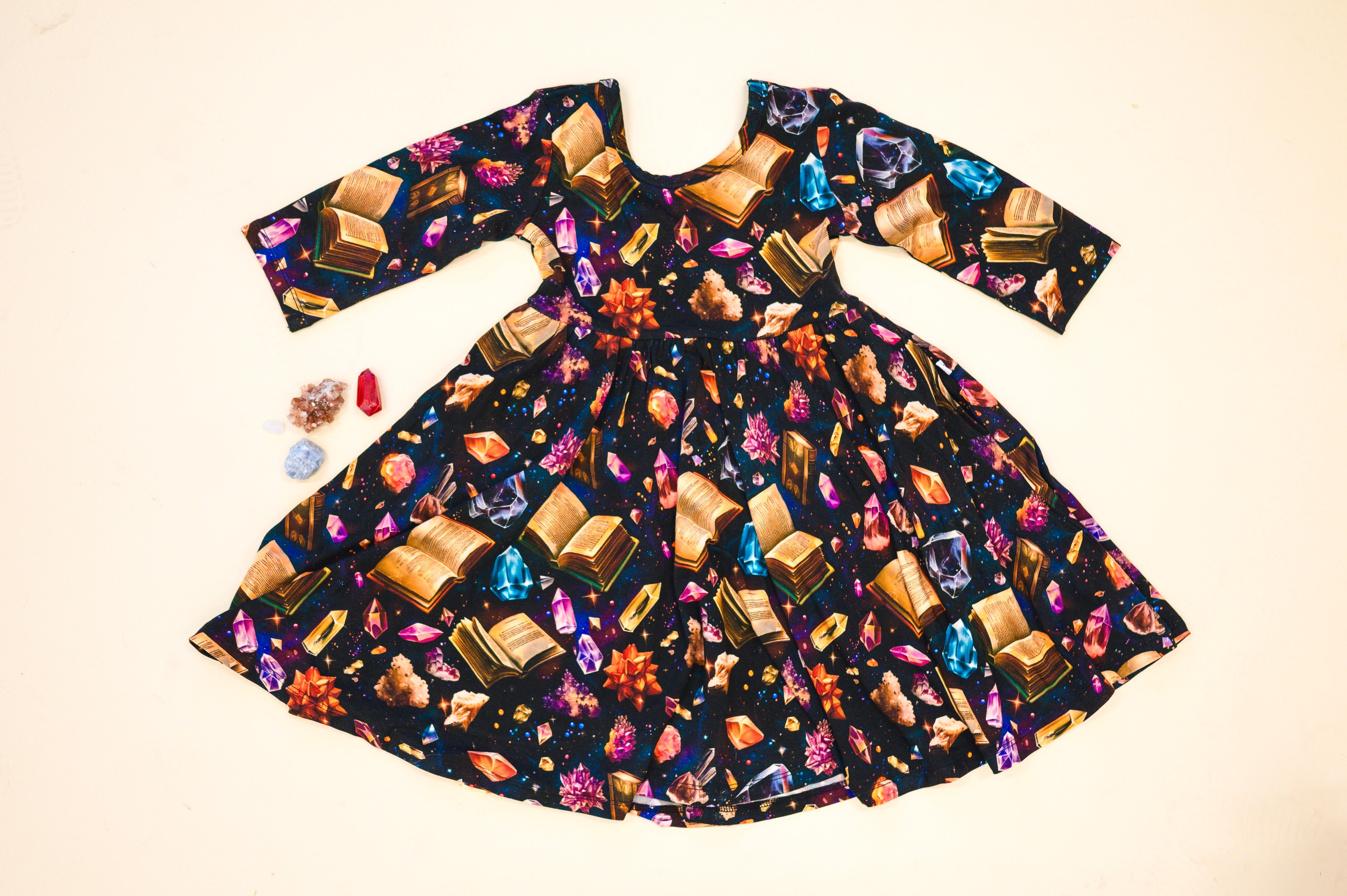 3/4 sleeve dress with a black background featuring a print of open books and colorful crystals.