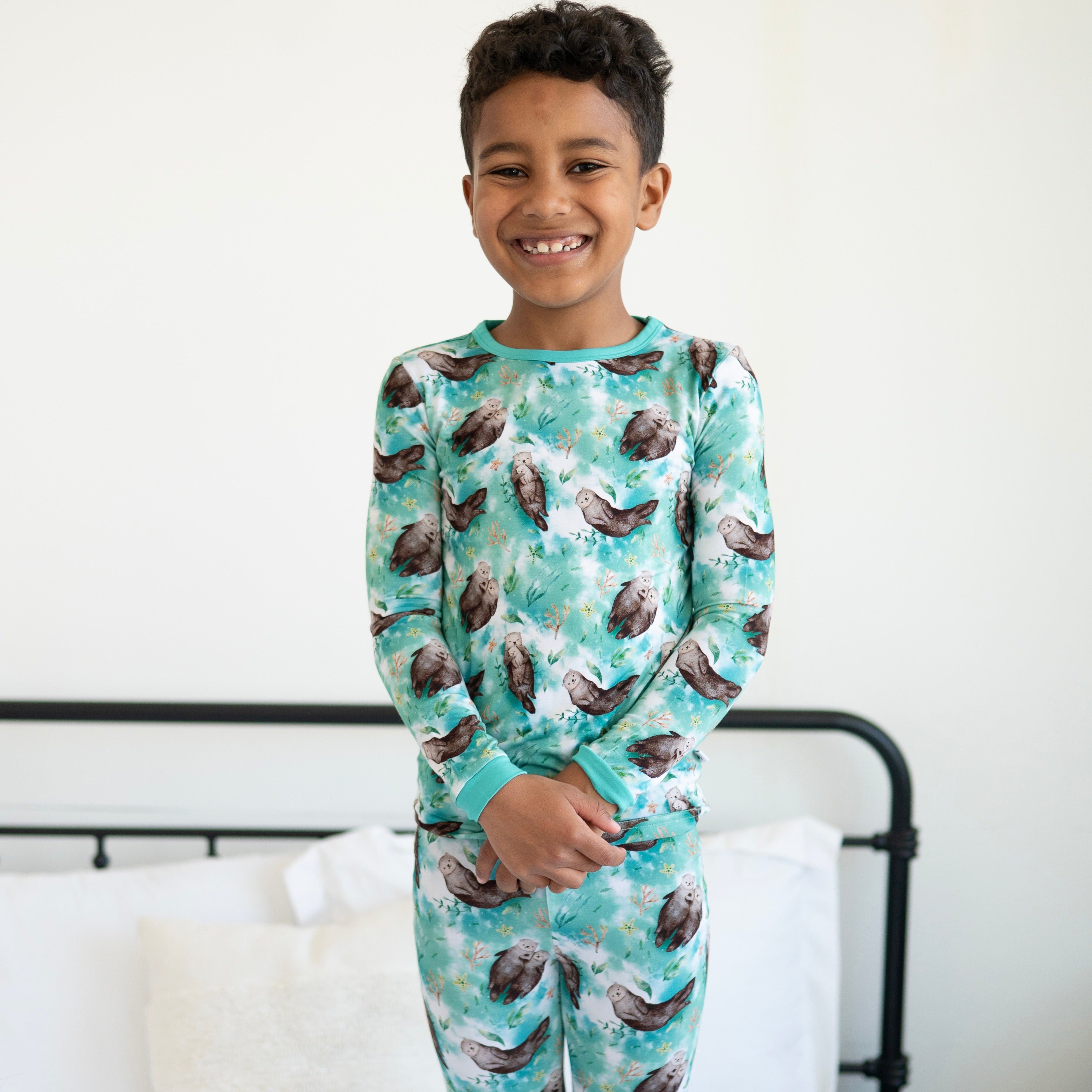 A young boy smiles wearing teal pajamas with an otter print.