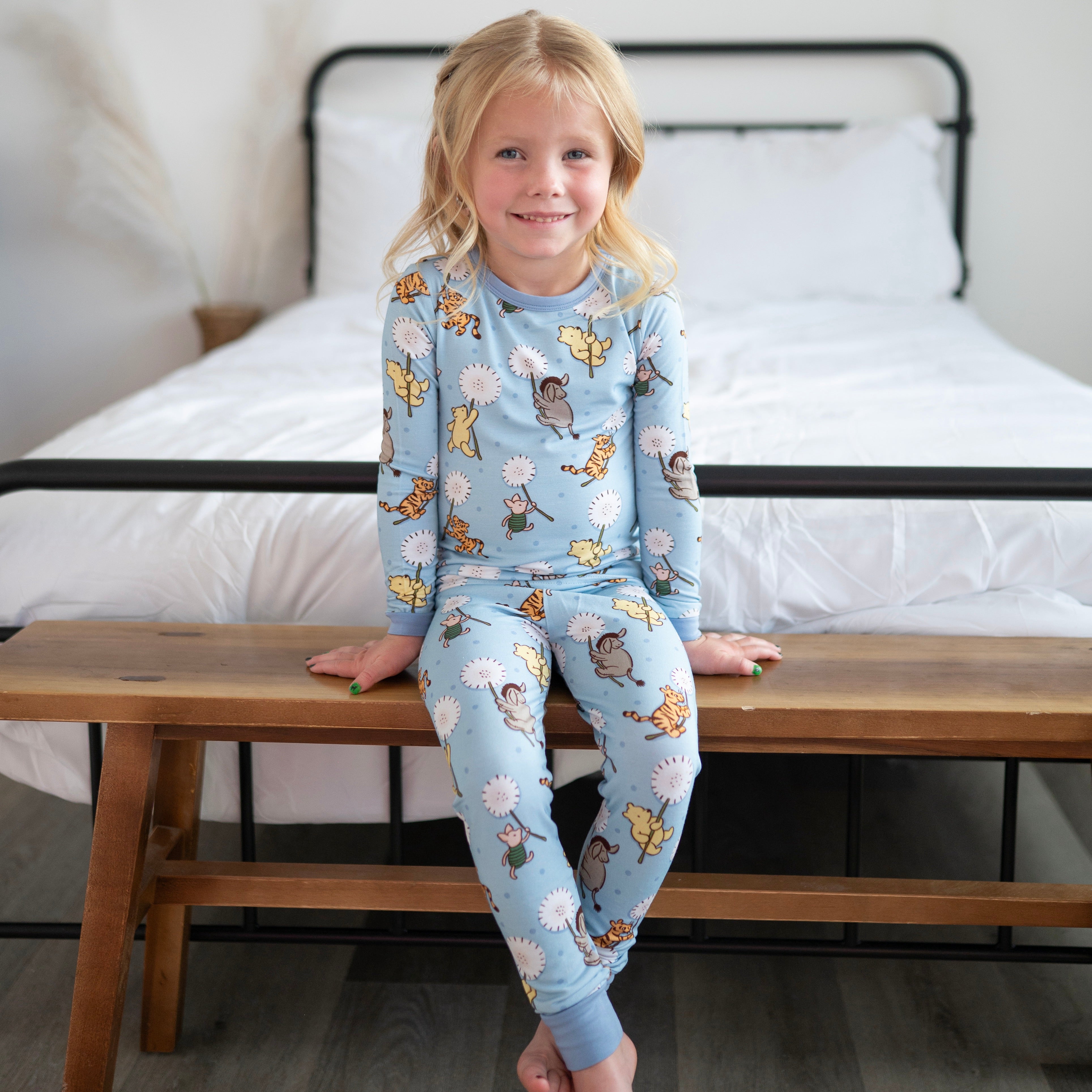 A young girl sits on a wooden bench wearing blue pajamas with a Winnie the Pooh print.