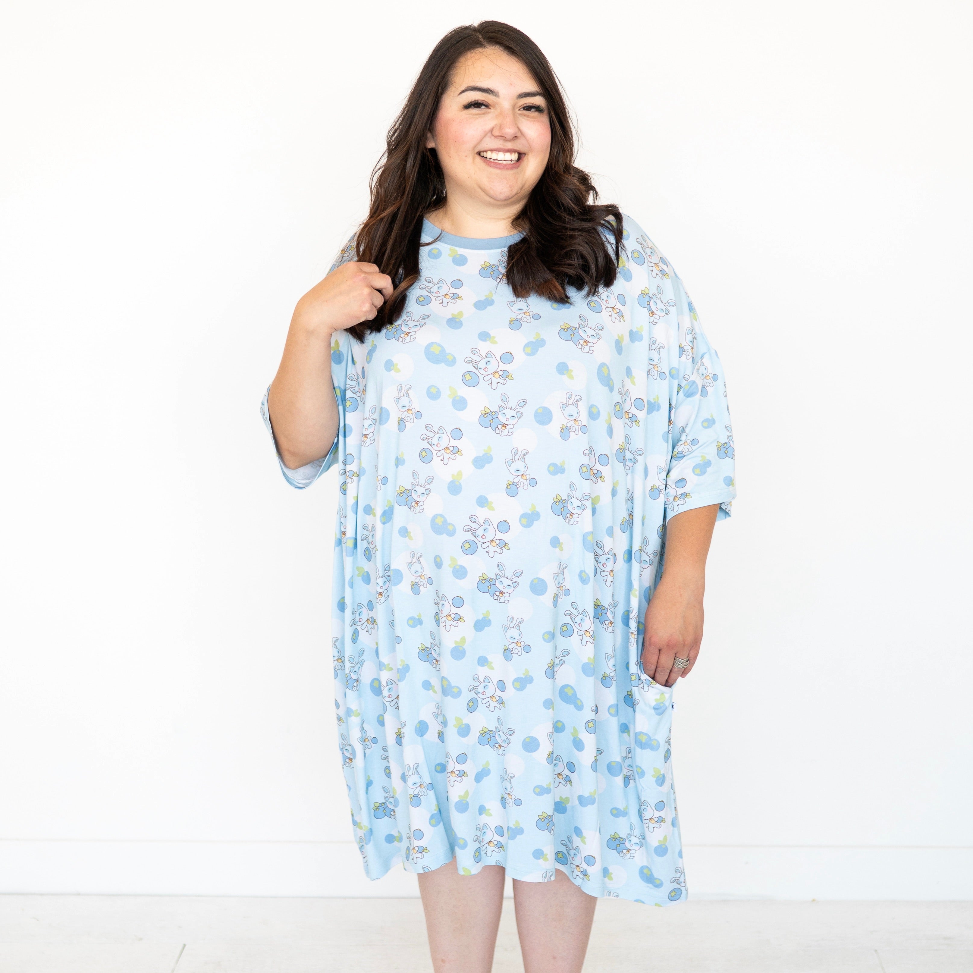A woman smiles wearing a light blue sleep tee with a blueberry and baby Neopets print.