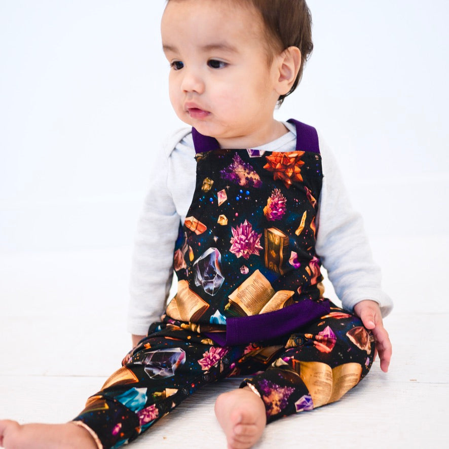 Baby wearing black overalls with a crystal and book print.