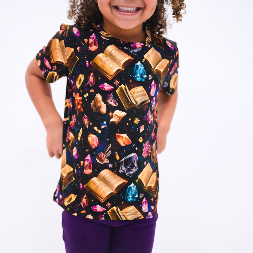 T-shirt with a black background featuring an all-over print of open books and colorful crystals.