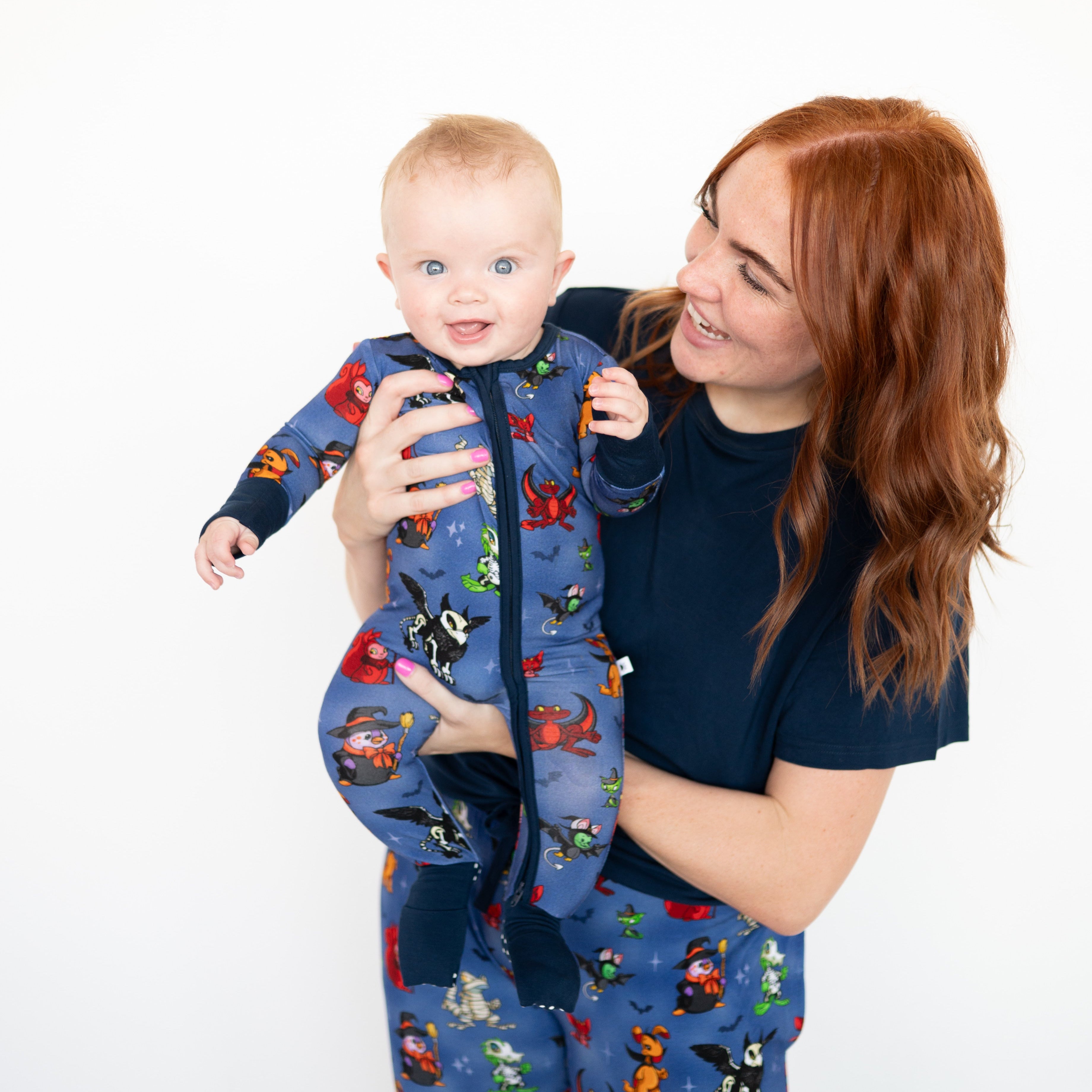 A woman holds a baby wearing a blue Halloween-themed pajama set.