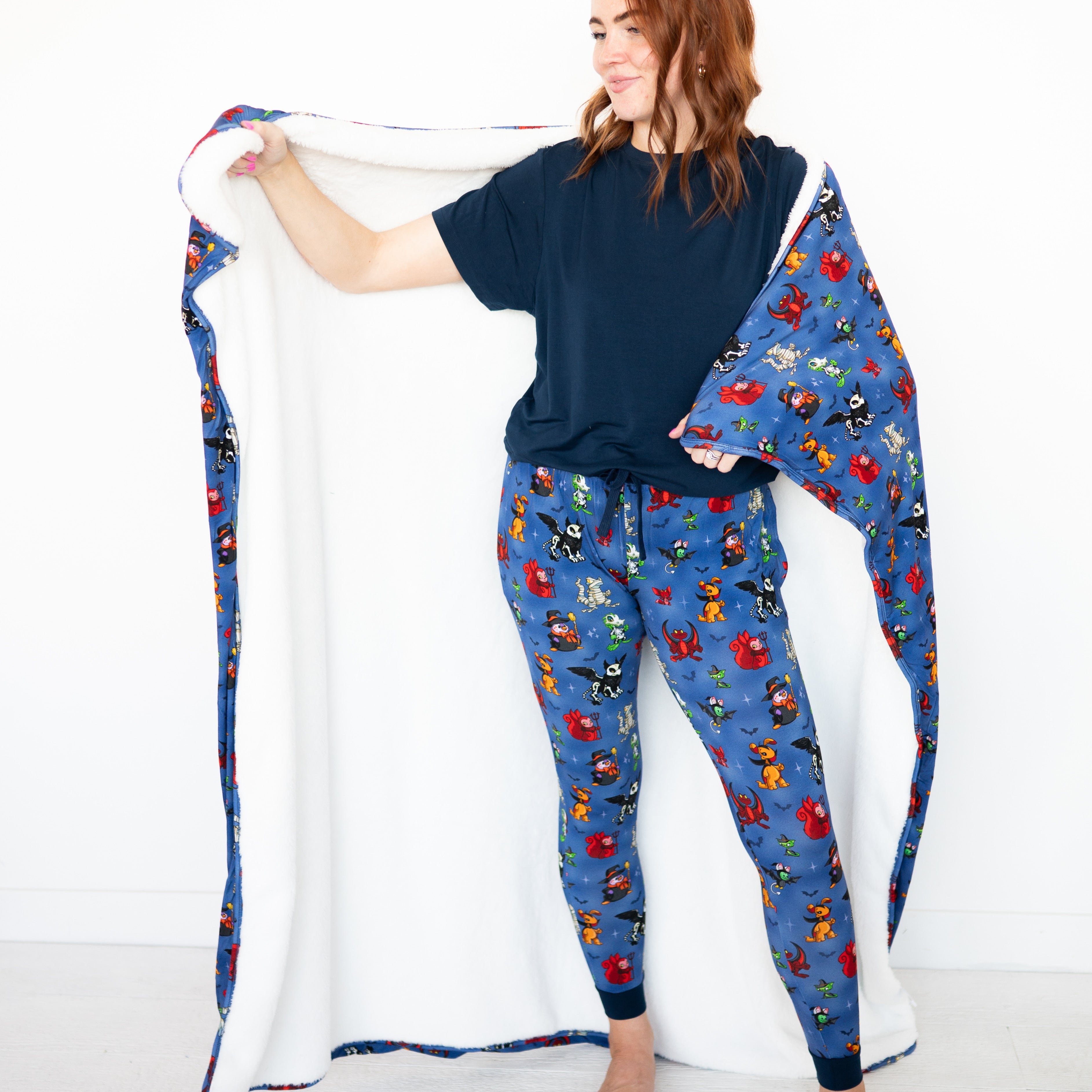 A woman wears blue pajamas with a Halloween Neopets print and holds a matching blanket.
