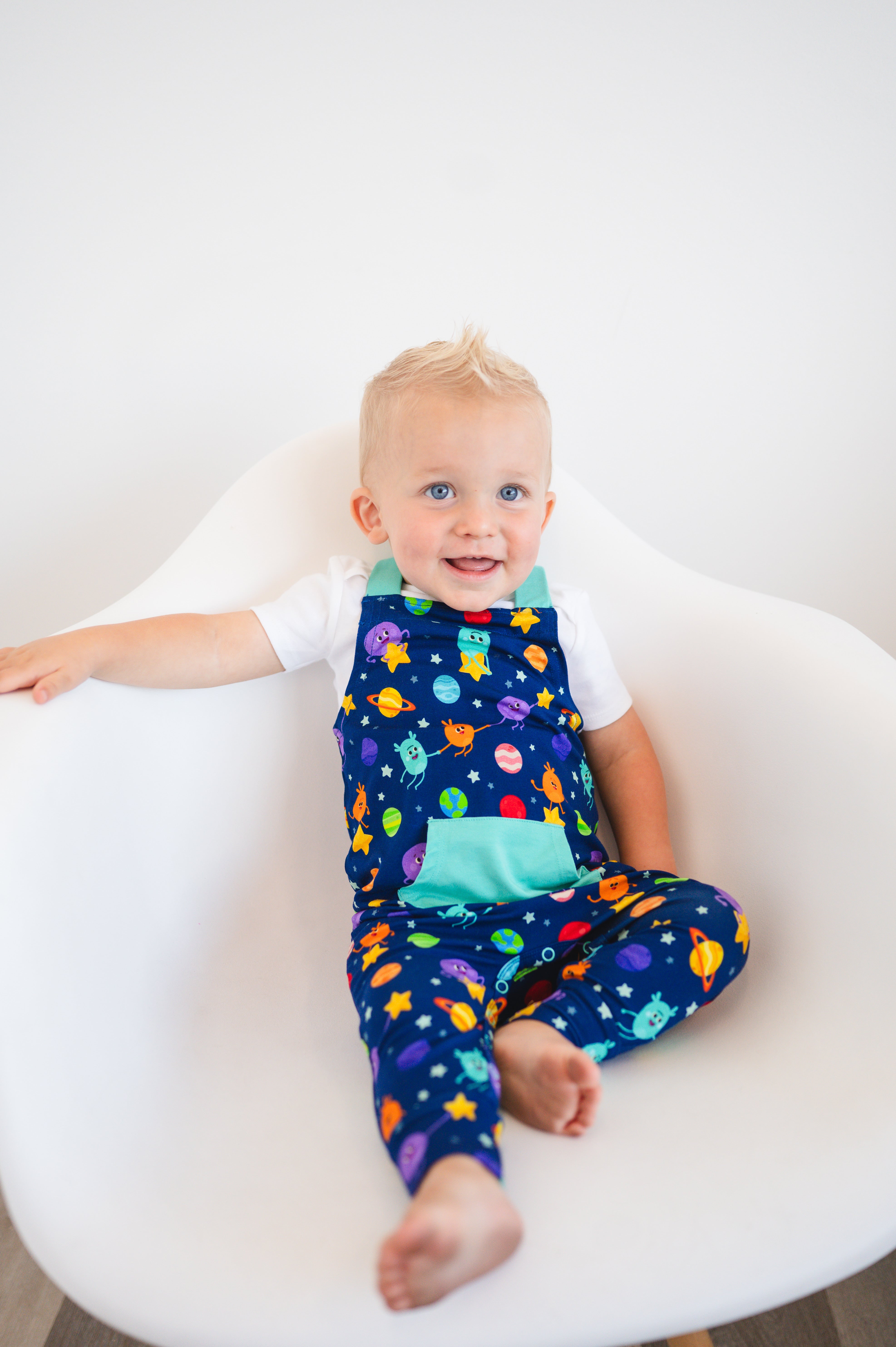 A baby boy wears blue overalls with a space-themed print.