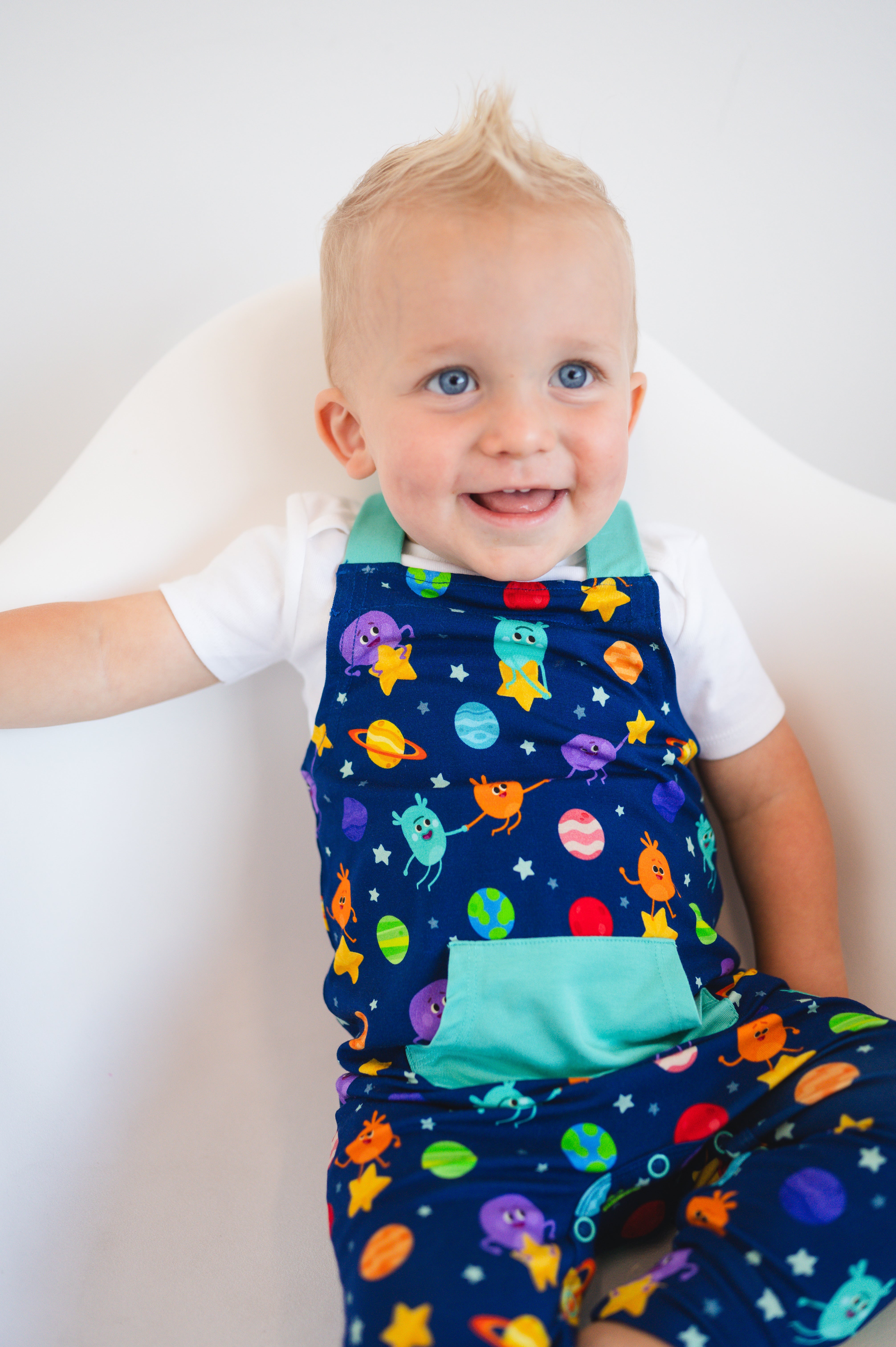 Baby in blue overalls with a space-themed print featuring planets and characters.