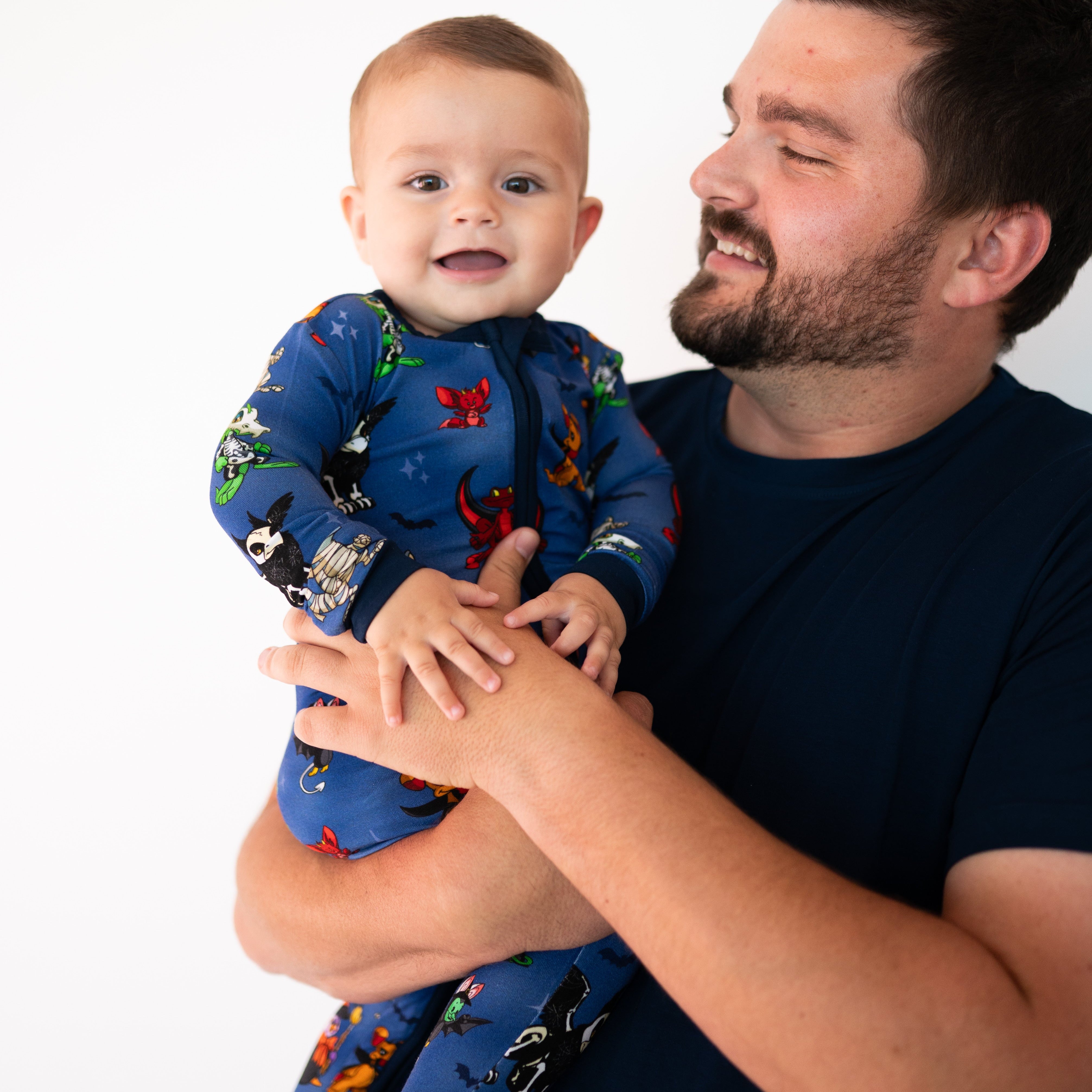 A father holds his baby, both wearing blue pajamas with a Halloween Neopets print.
