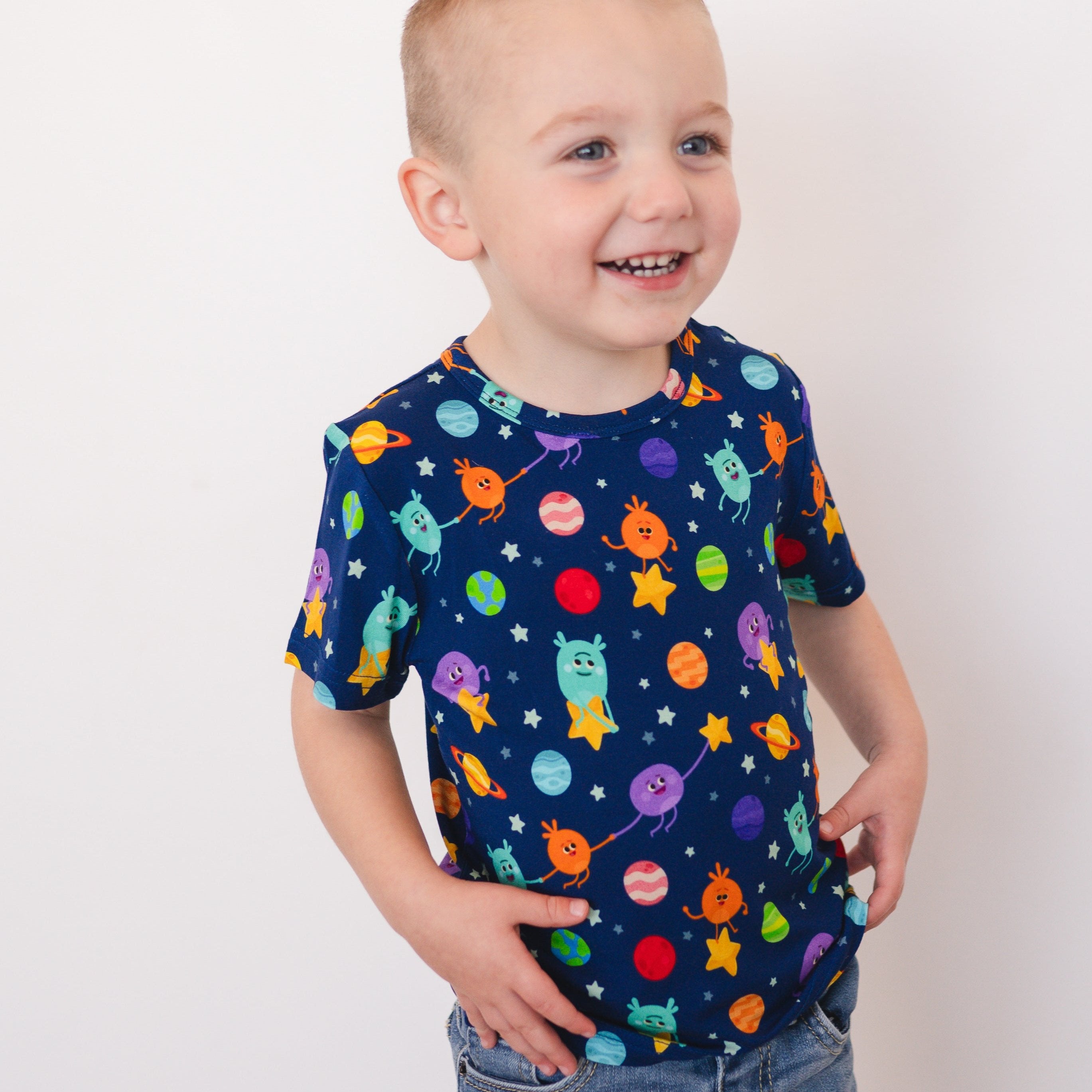 A young boy wears a navy blue t-shirt with a colorful space-themed print.