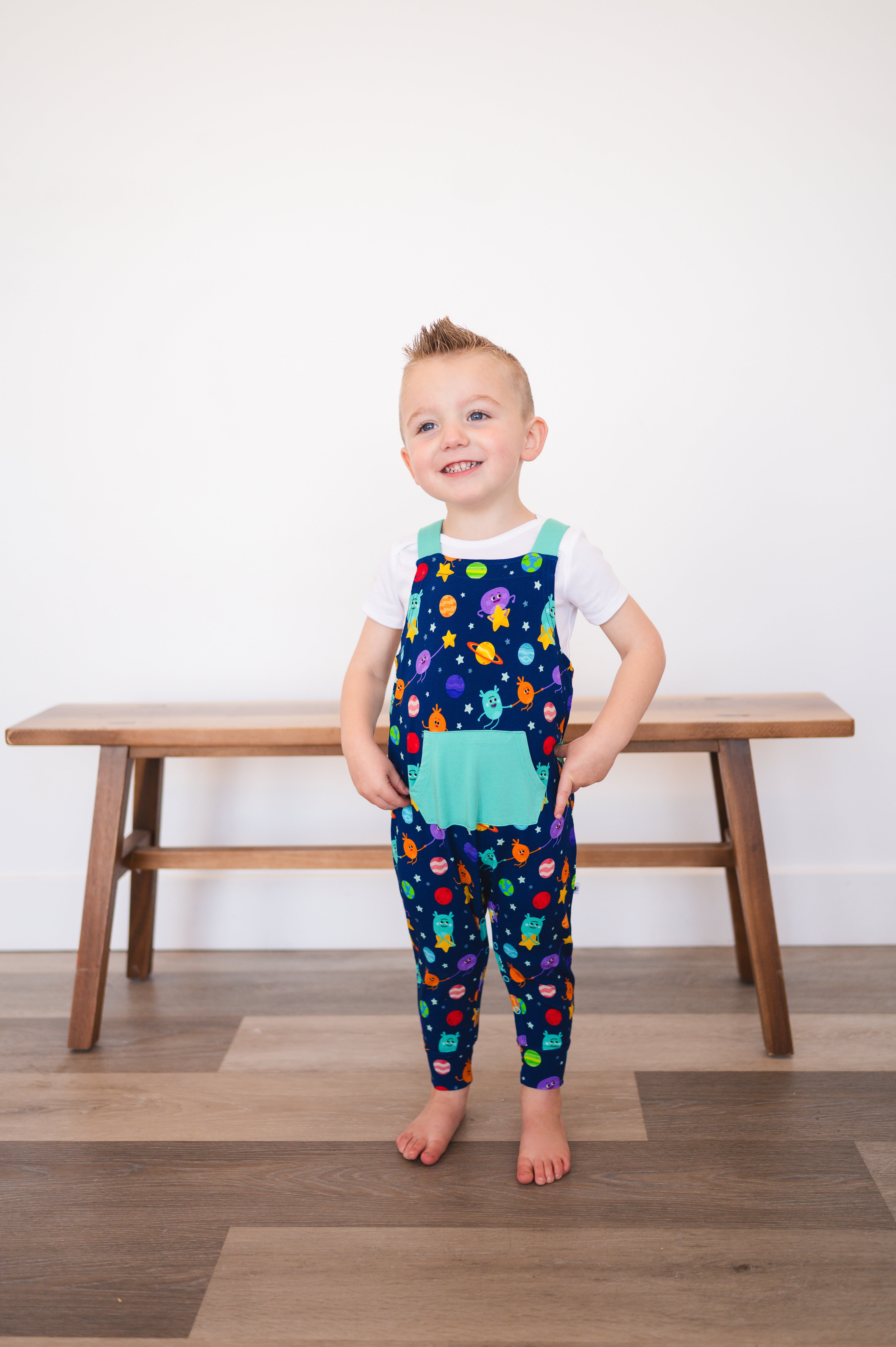 A young boy wears blue overalls with a space-themed print.