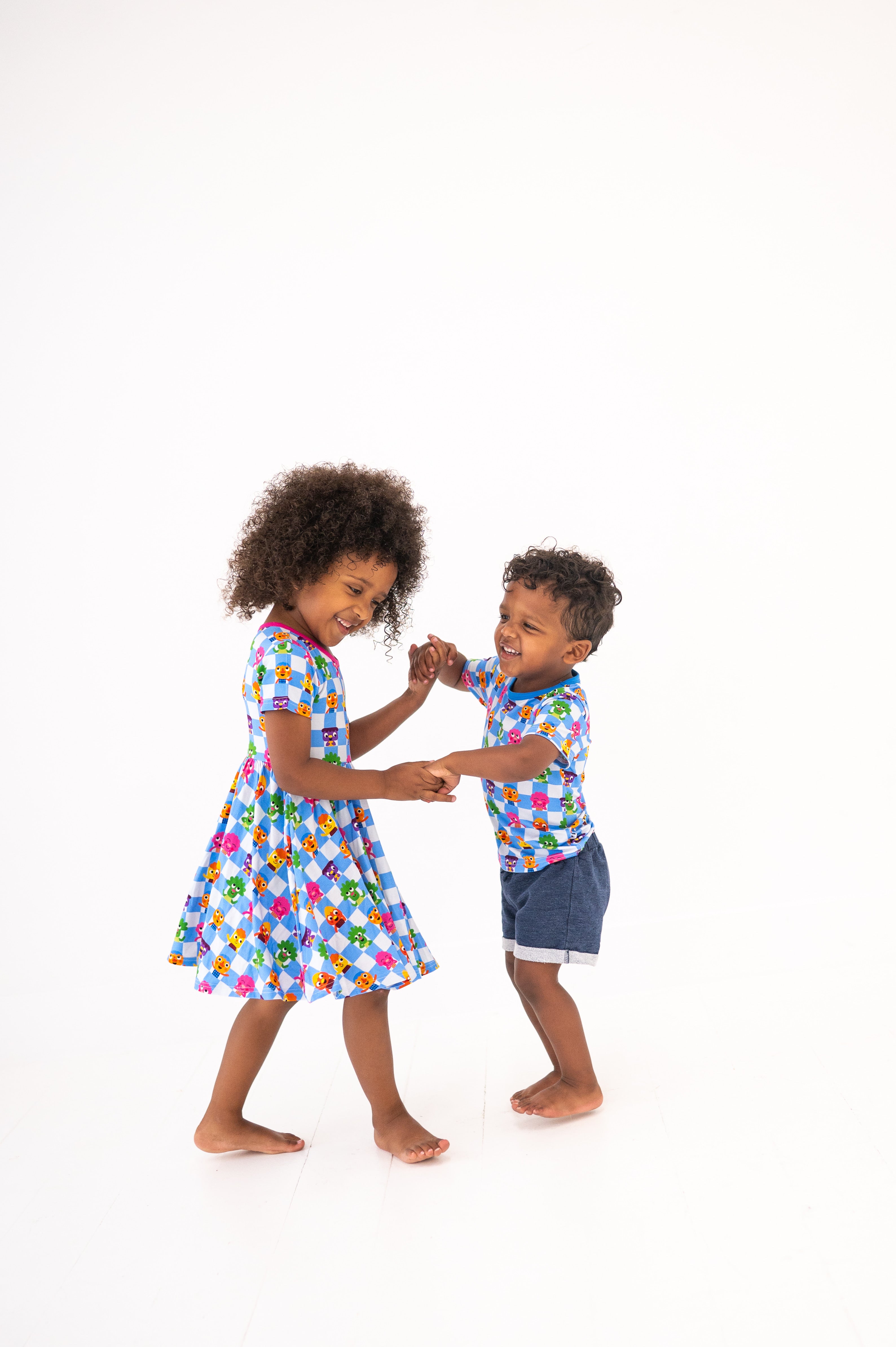 Two children in matching blue checkered outfits with cartoon characters dance.