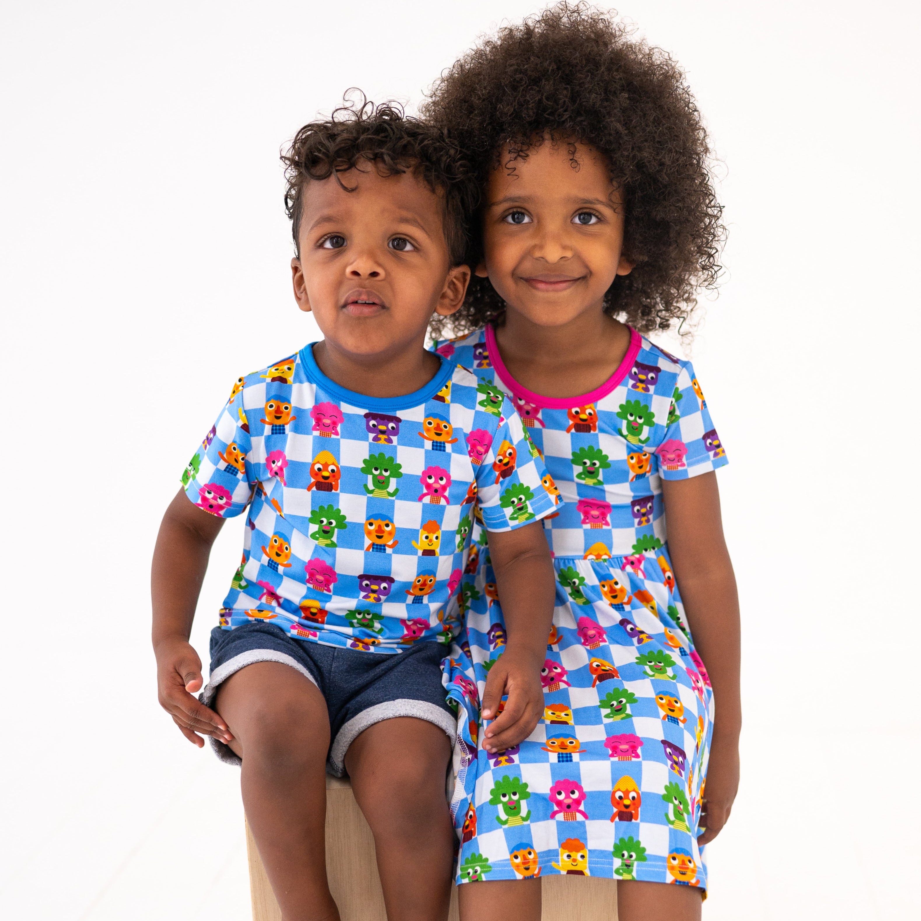 Two children wearing matching blue checkered t-shirts with cartoon characters.