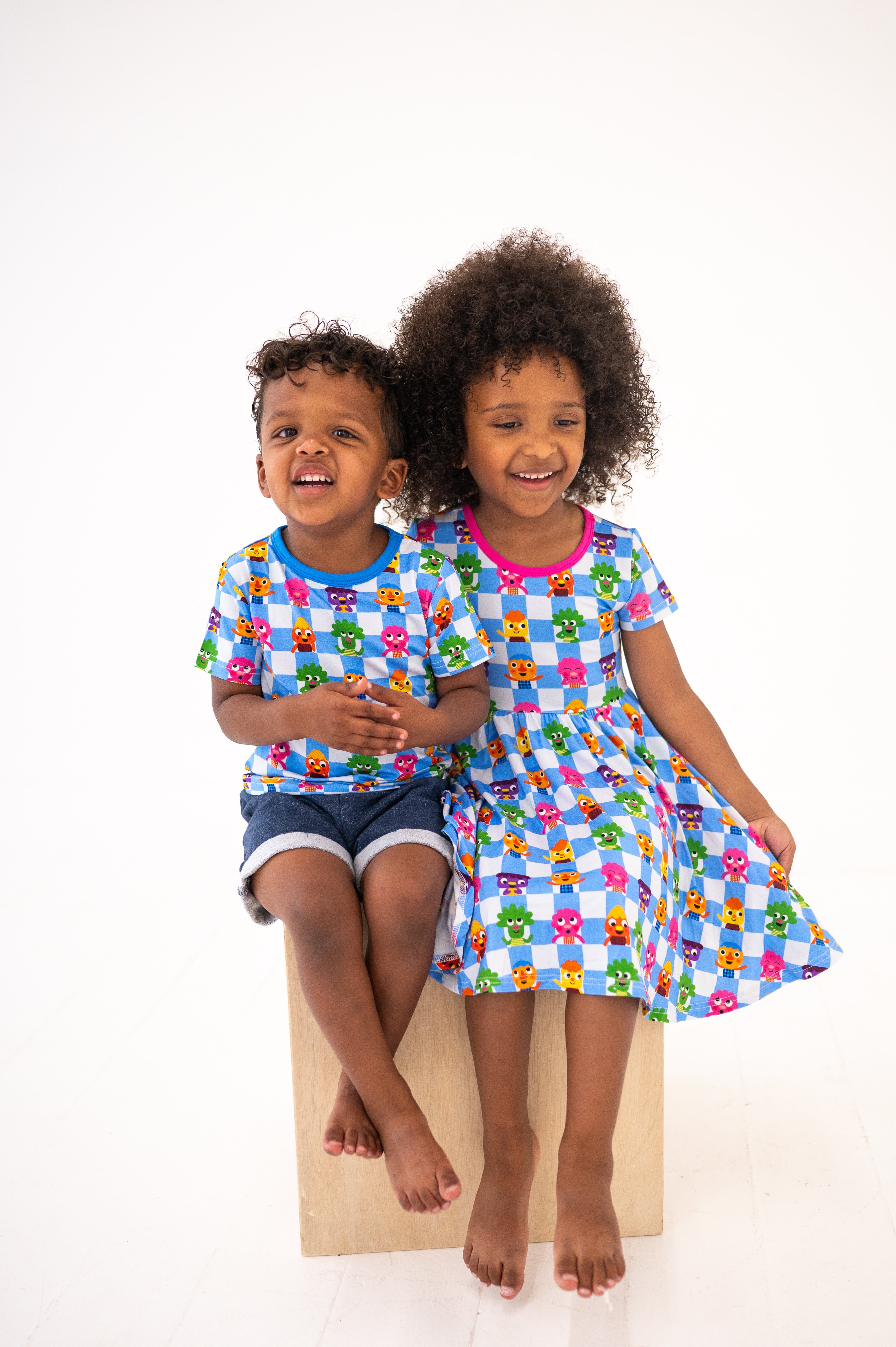 Two children in matching blue checkered shirts with cartoon characters, one boy and one girl.