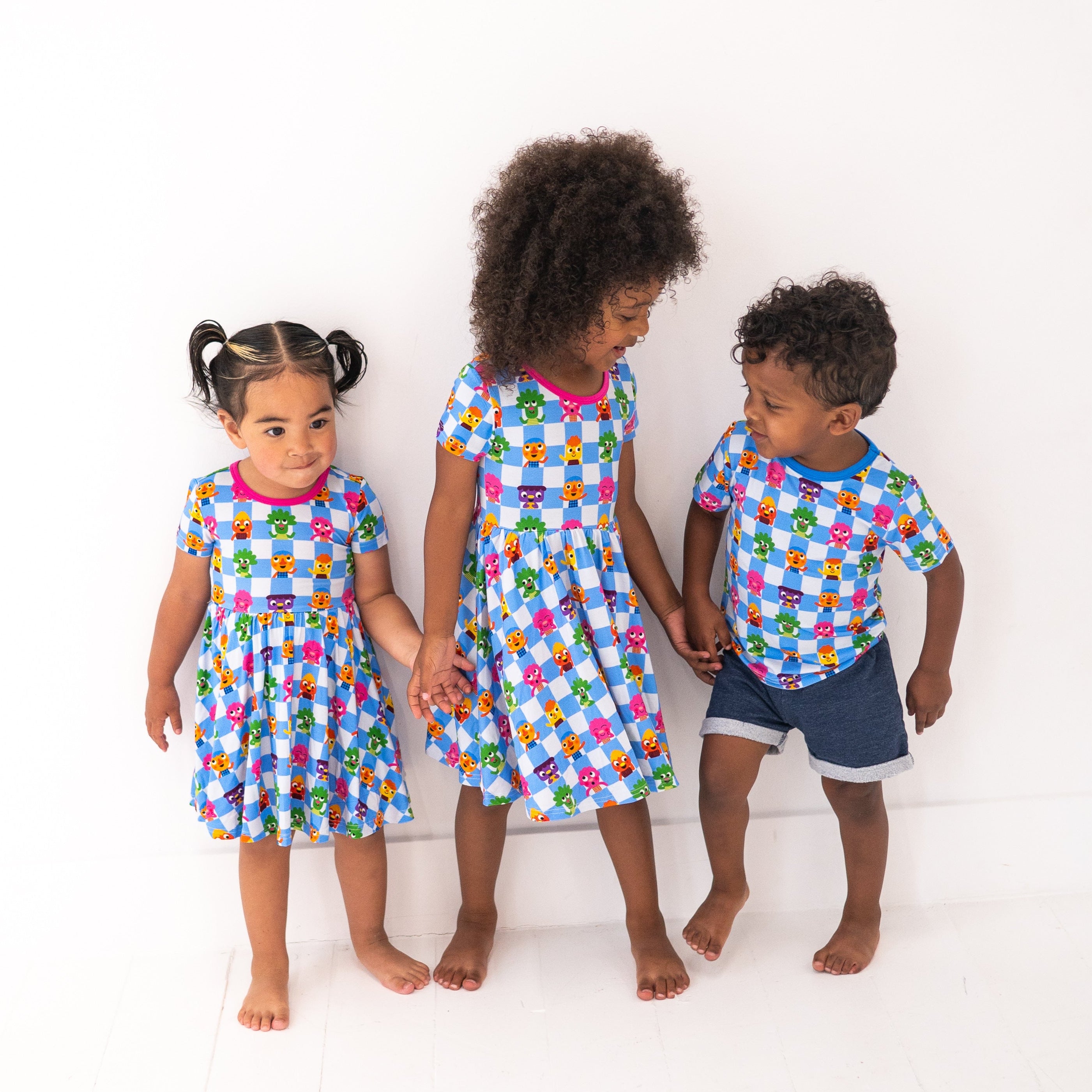 Three children in matching blue checkered shirts with cartoon characters and one boy in denim shorts.